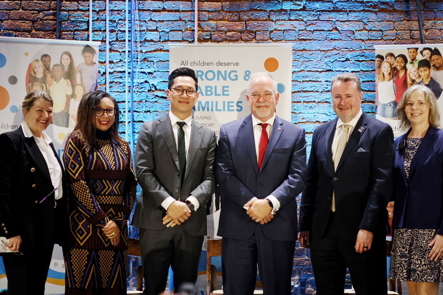 Six professionals pose together at a Strong and Stable Families event in a modern office setting.