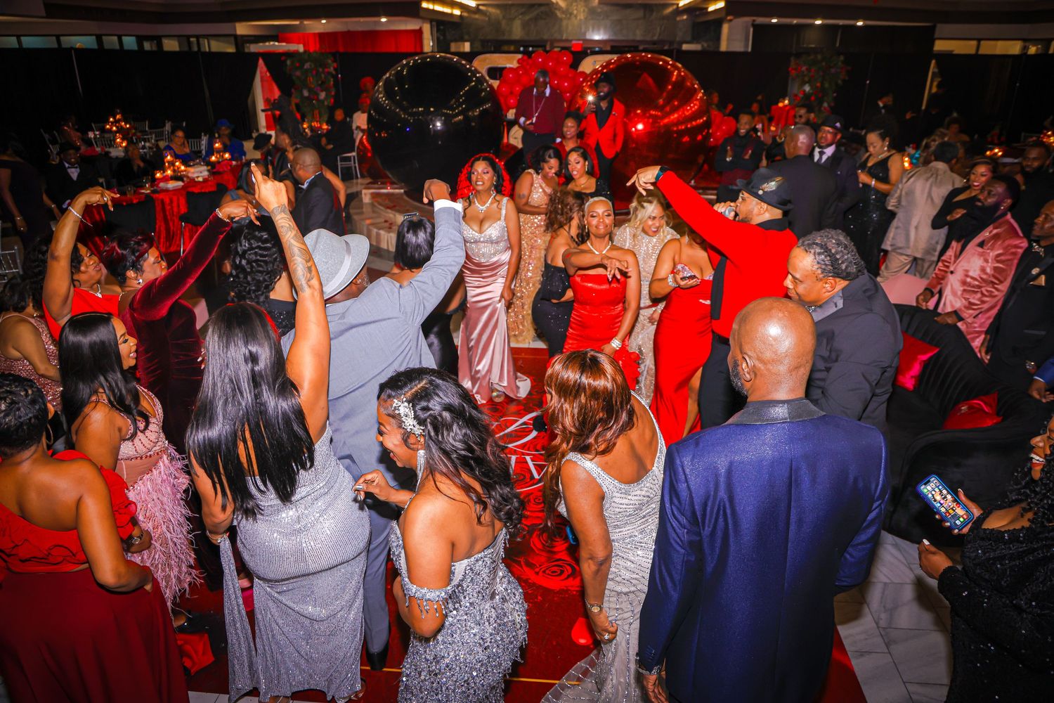 Elegant guests in red and silver formal attire dancing and celebrating at a glamorous evening gala event.