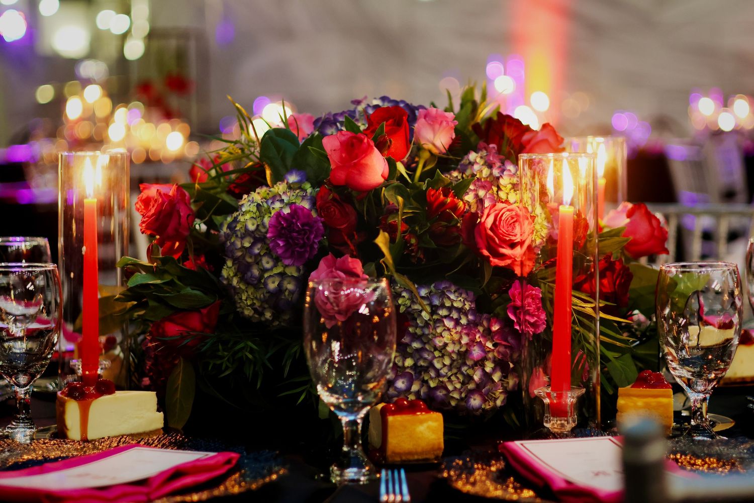 Elegant wedding centerpiece with red roses, purple hydrangeas, and glowing red candles on a dark reception table.