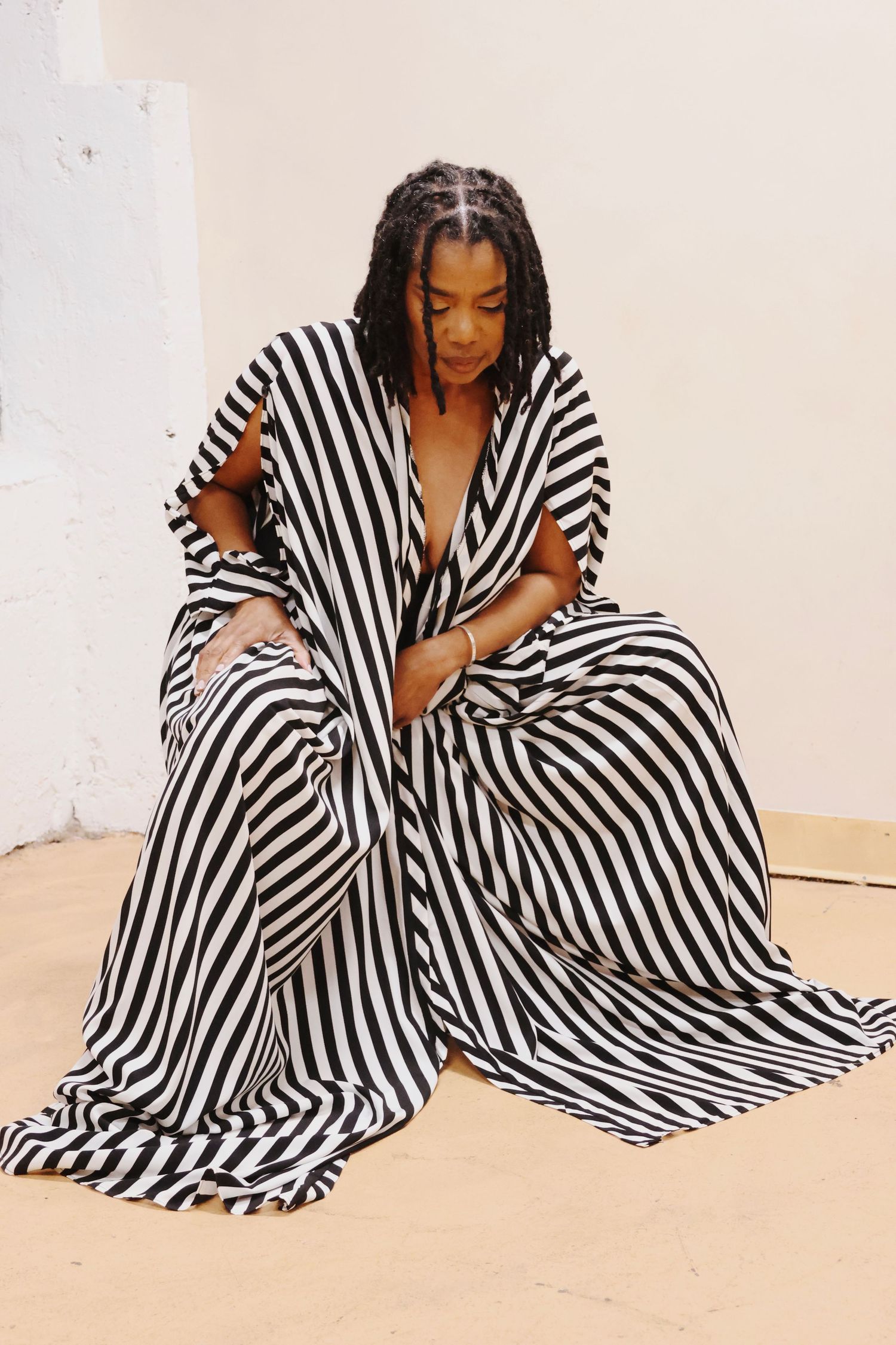 A Black woman poses in a dramatic black and white striped oversized gown on a light-colored floor.