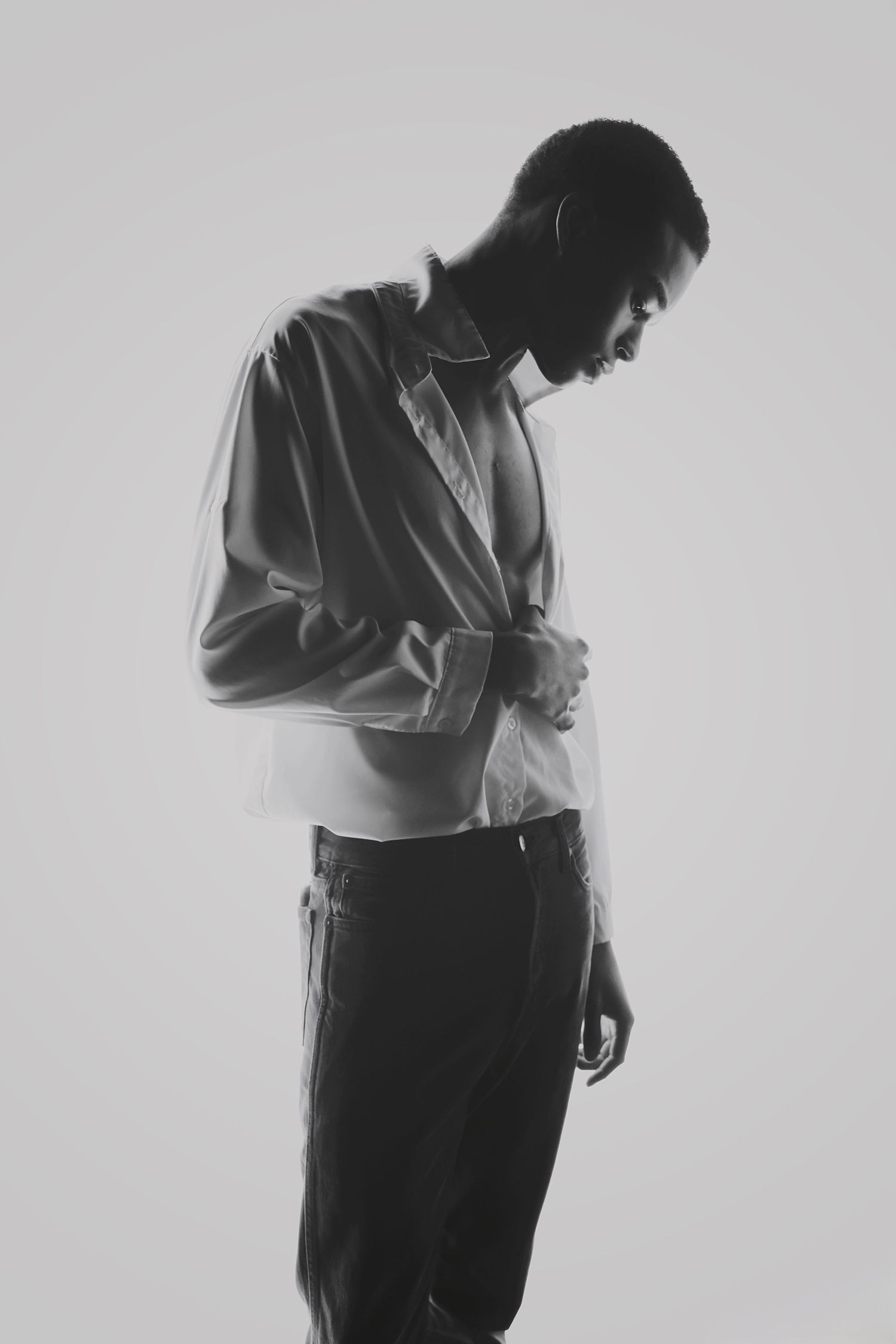 Black and white portrait of man in white shirt looking down, minimalist studio fashion photography.