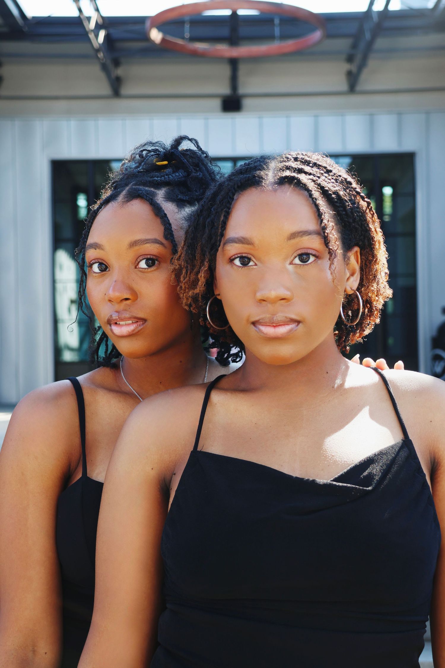 Two young Black women in matching black outfits posing together outdoors, portrait photography.