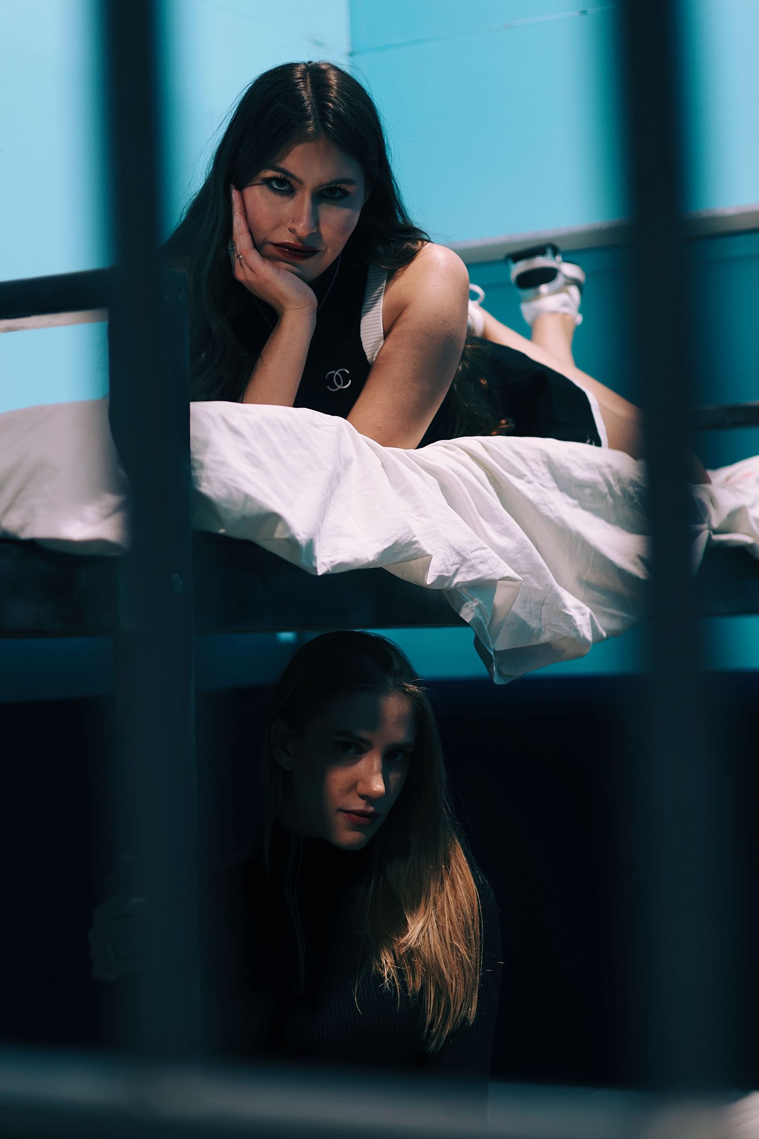Two women in a jail cell, one lying on a bunk bed and another sitting below, in a dramatic blue-lit scene.