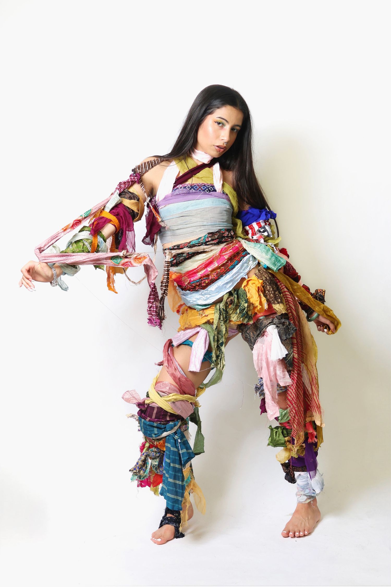 Woman wearing a colorful patchwork outfit made of fabric scraps, posing dynamically against a white background.