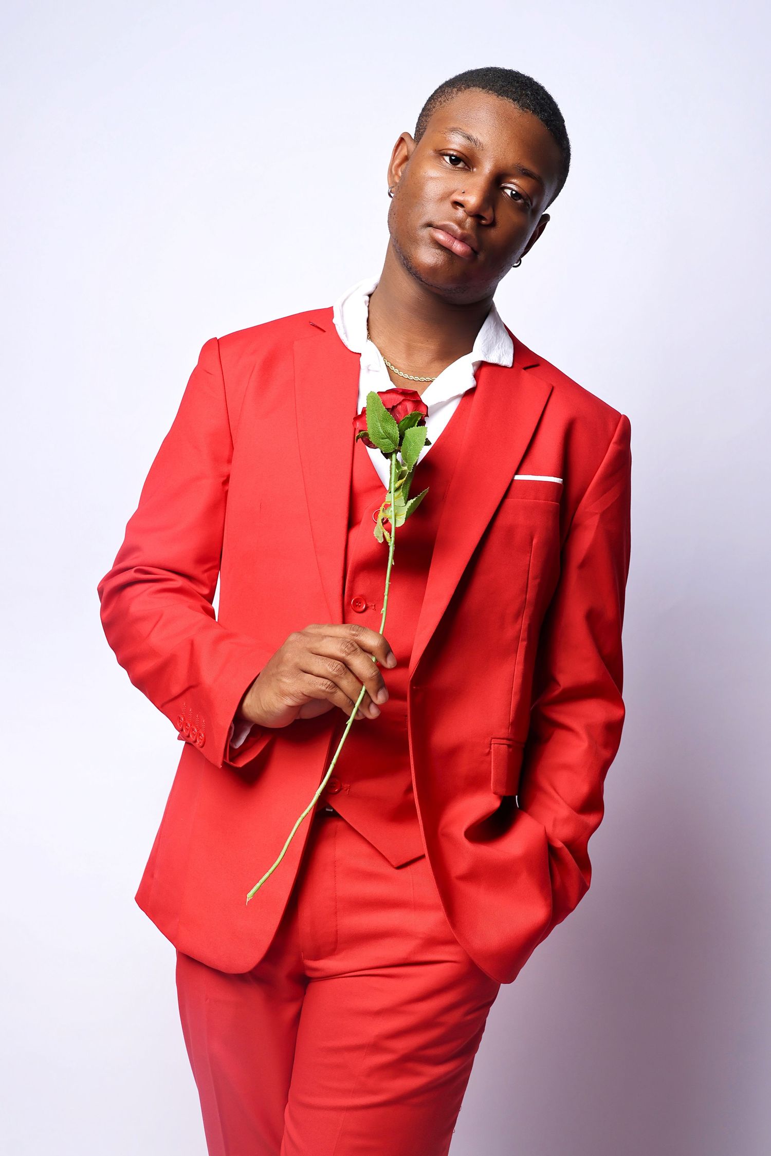 Young man in a red three-piece suit holding a single red rose against a white background.