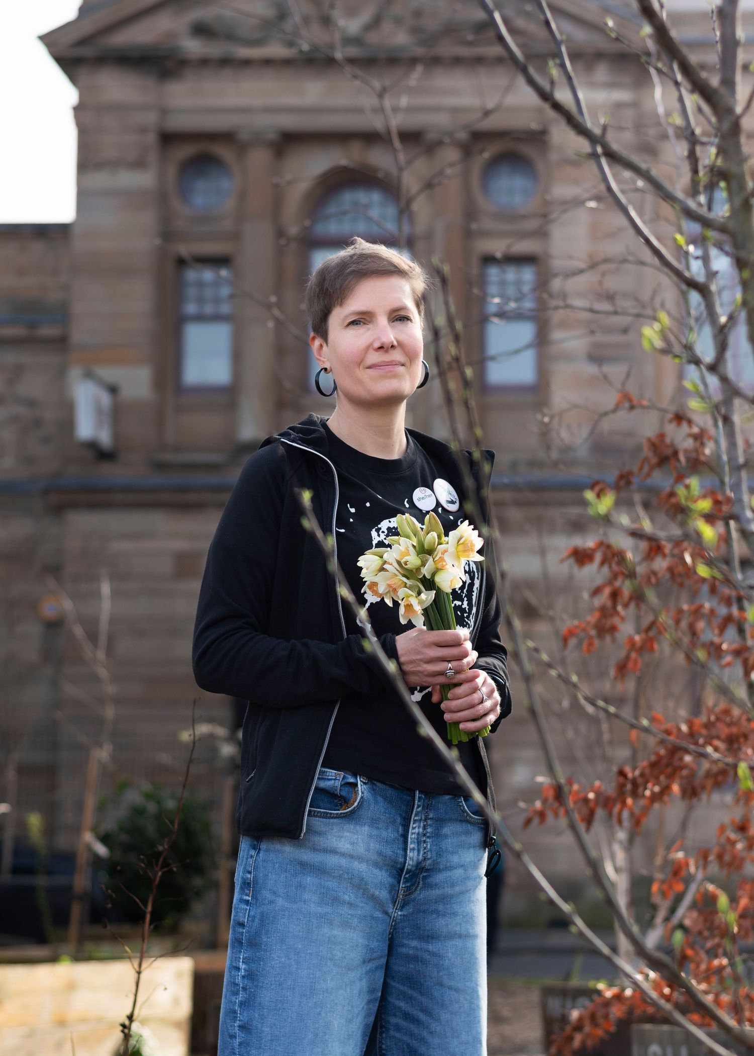 A woman holding flowers, standing in a garden outside Glasgow Women's Library