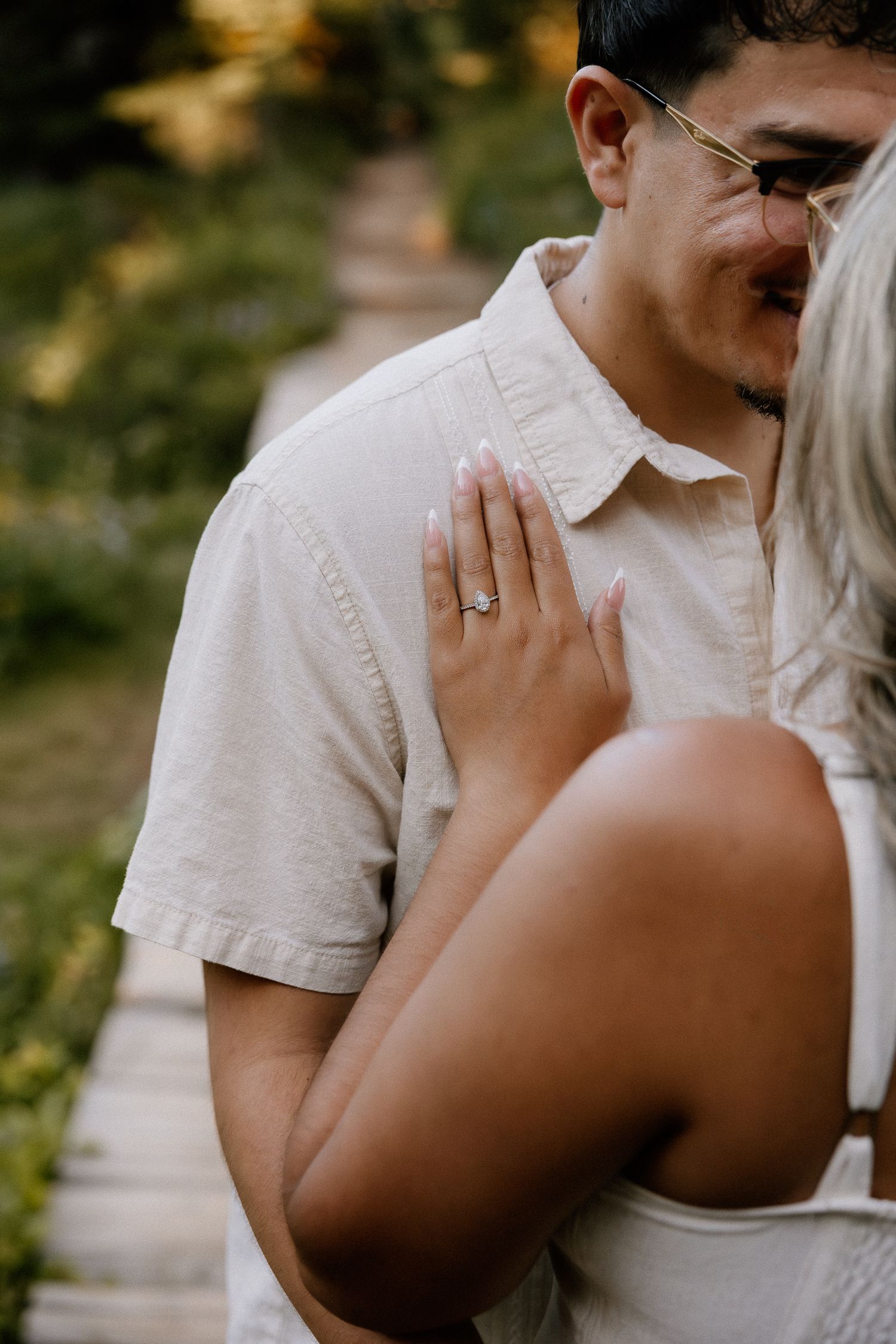 Close-up of a woman showing her engagement ring while embracing her partner outdoors in a garden.