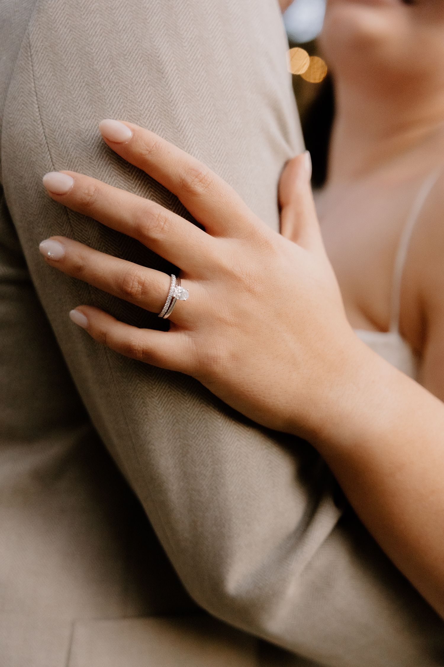 Close-up of bride's hand with wedding ring resting on groom's tan suit jacket.