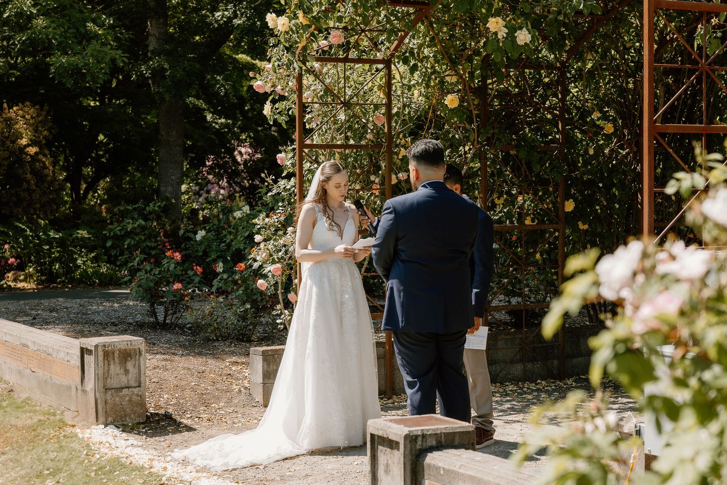 Bride and groom exchanging vows at an outdoor garden wedding ceremony with floral arbor.
