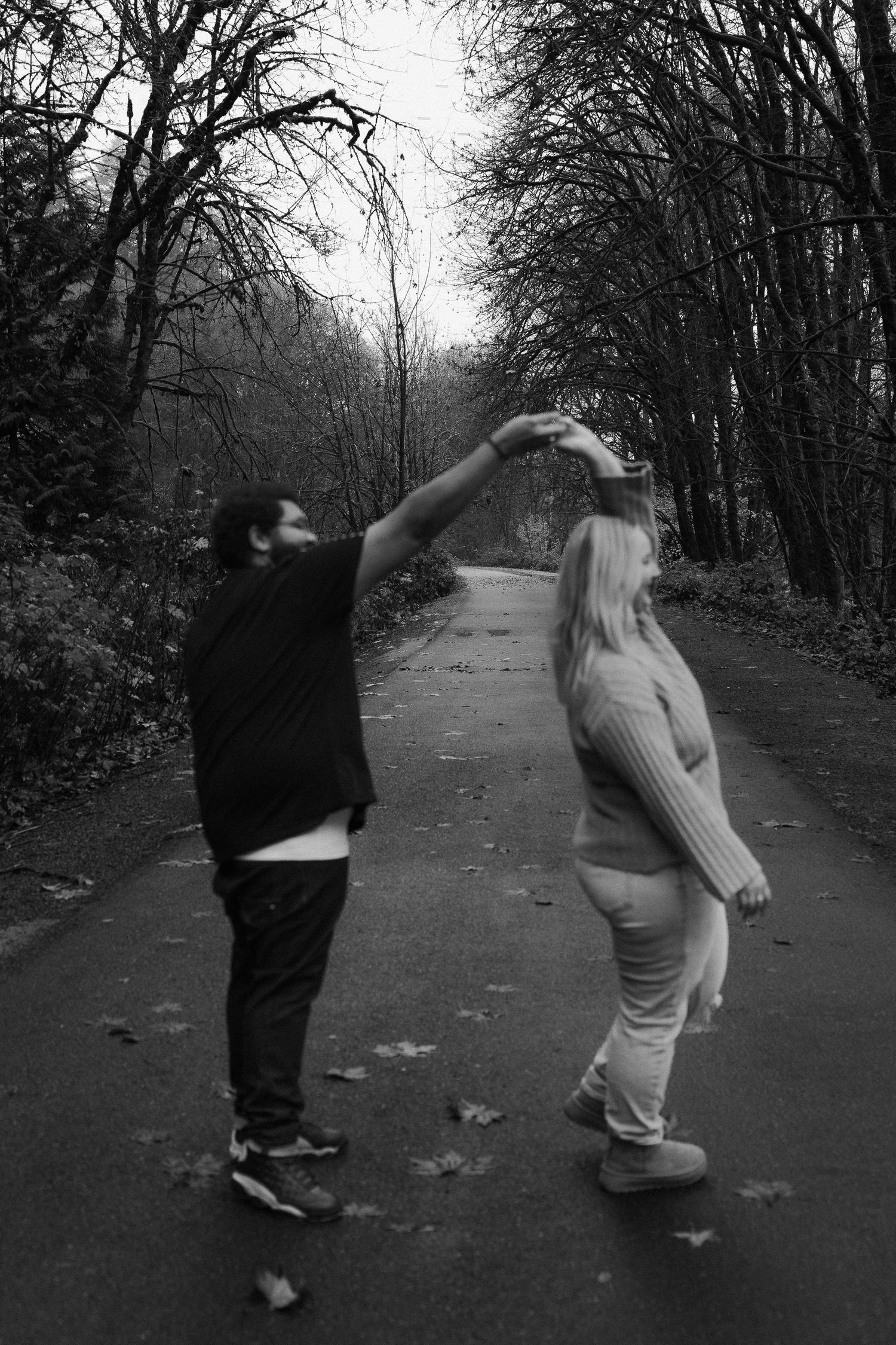 Black and white photo of couple dancing on a tree-lined path in autumn.