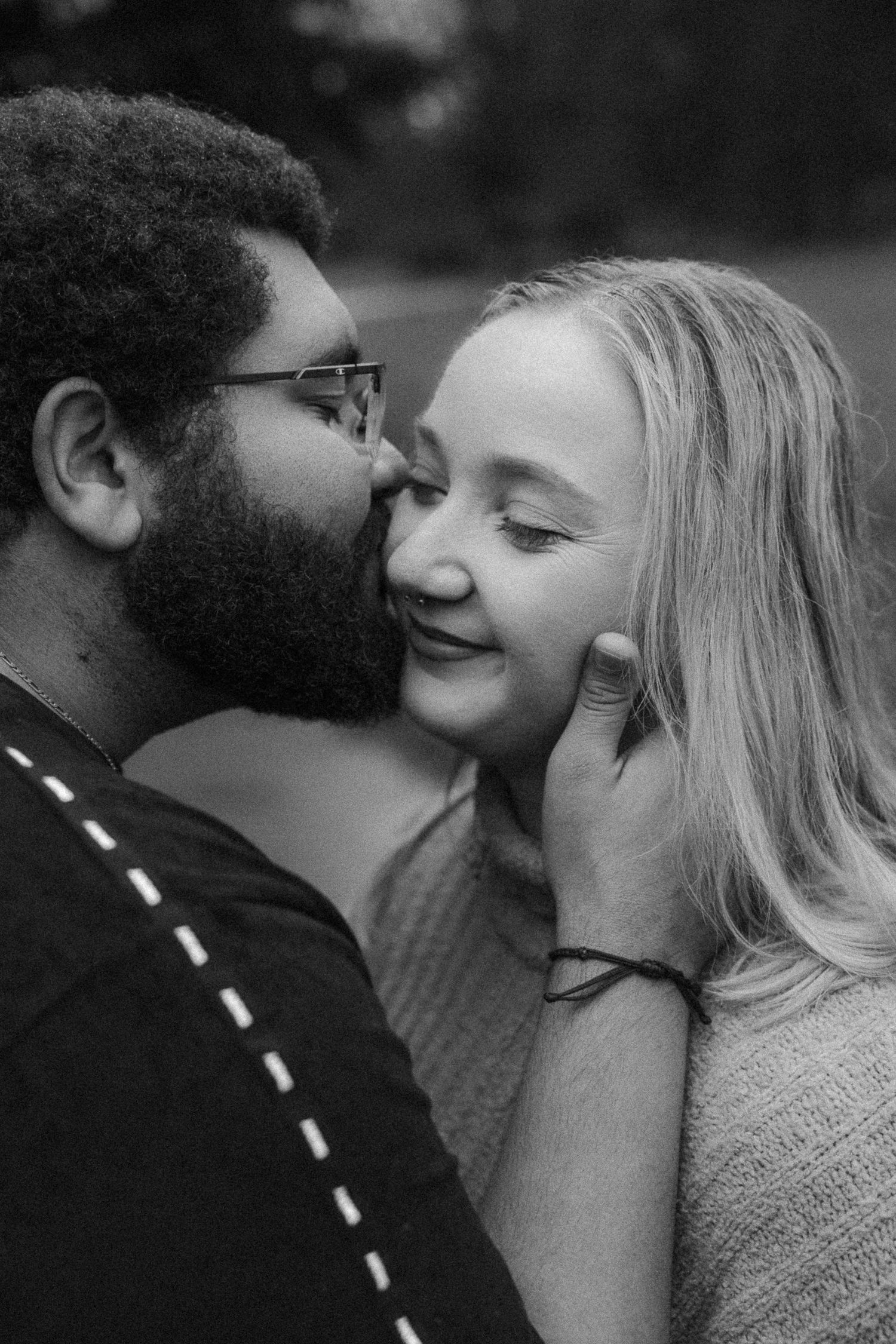 Black and white photo of a bearded man gently kissing a smiling blonde woman on the cheek.