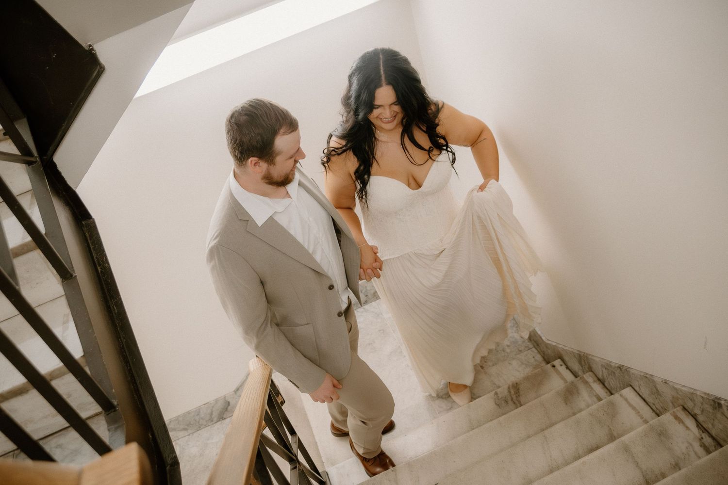 Aerial view of bride and groom walking hand-in-hand up elegant staircase together.