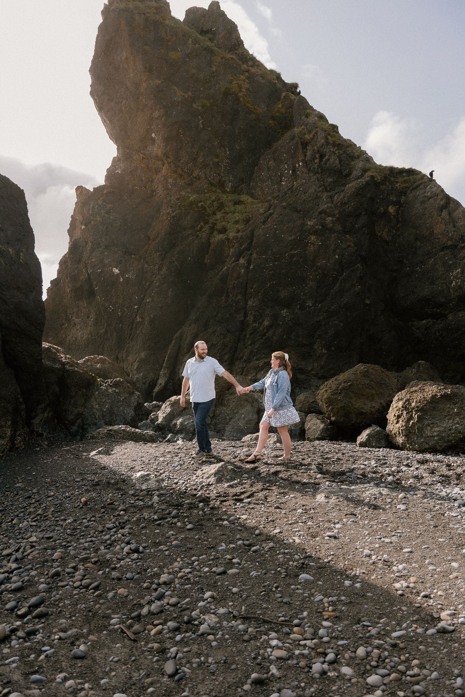 Couple holding hands walking on Ruby beach with dramatic cliffs in background.