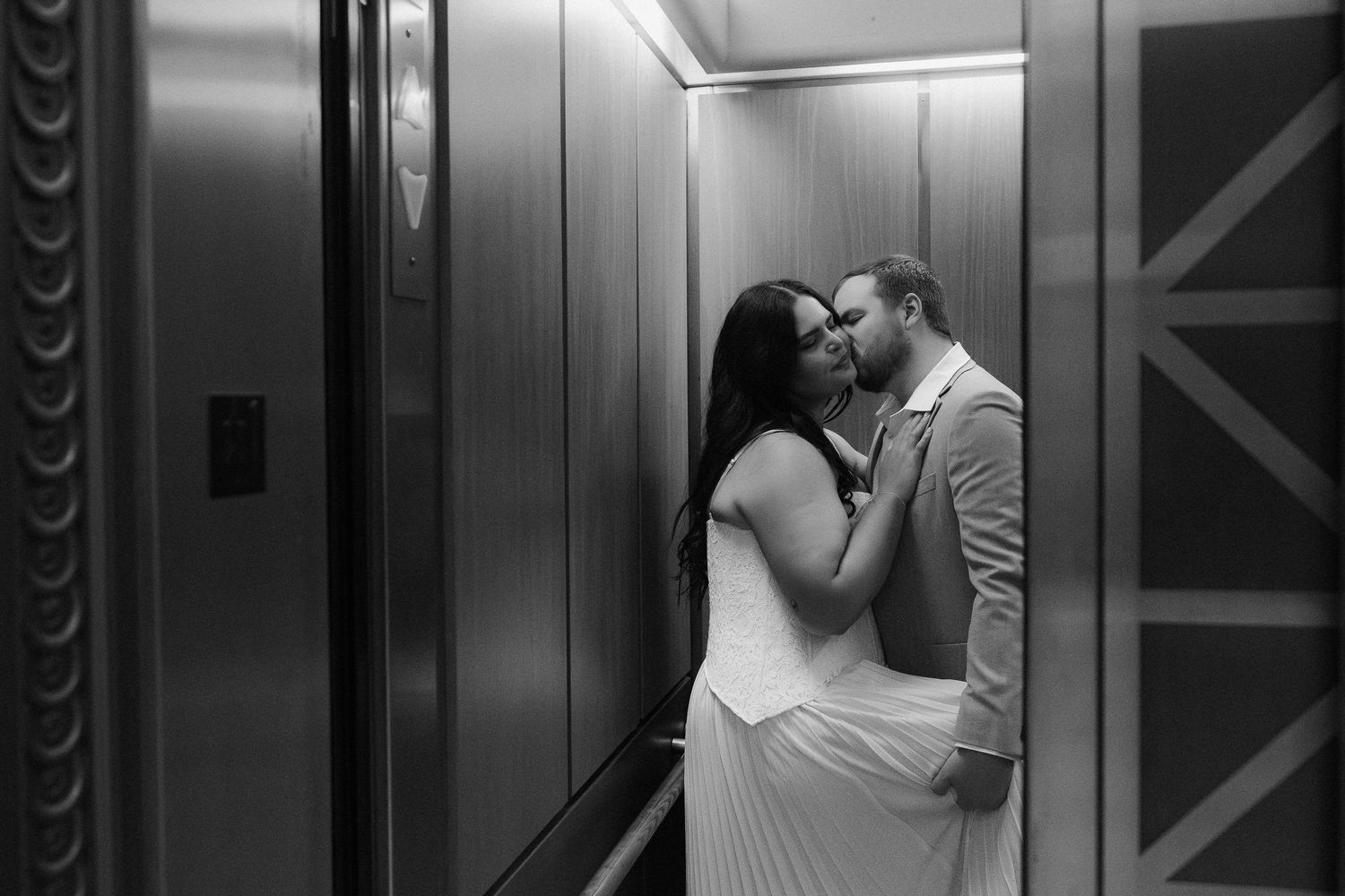 Black and white photo of bride and groom sharing a kiss inside a elegant elevator.