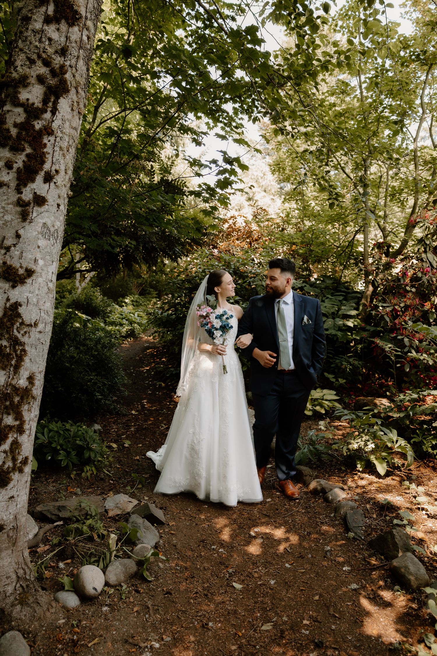 Bride and groom walking together through a lush green forest garden on their wedding day.