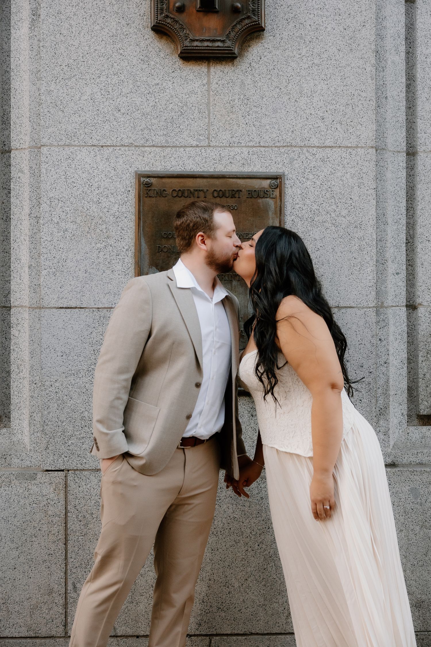 Couple shares a kiss outside King County Courthouse, groom in tan suit and bride in white dress.