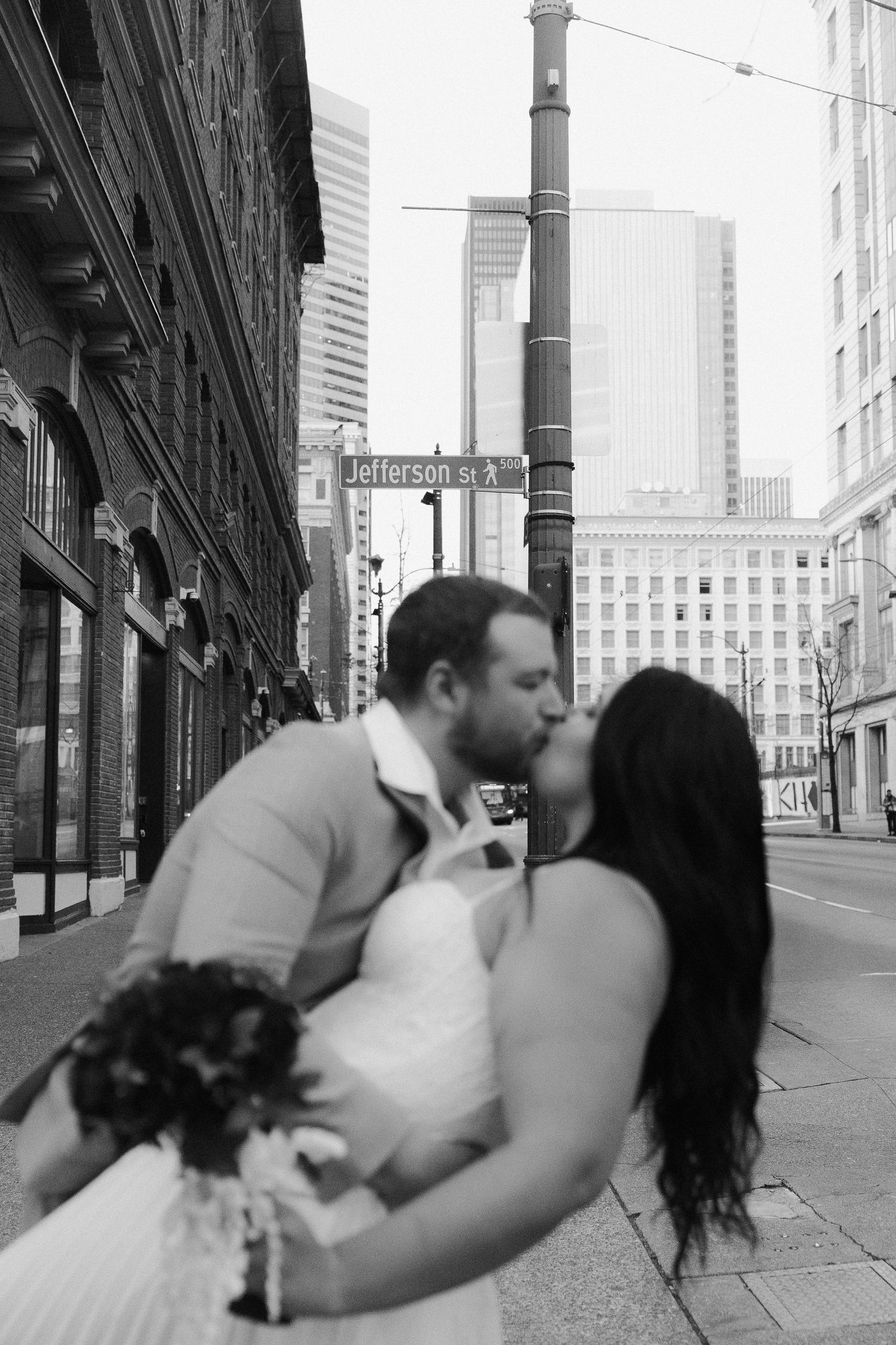 Black and white photo of bride and groom kissing on Jefferson Street in urban setting.
