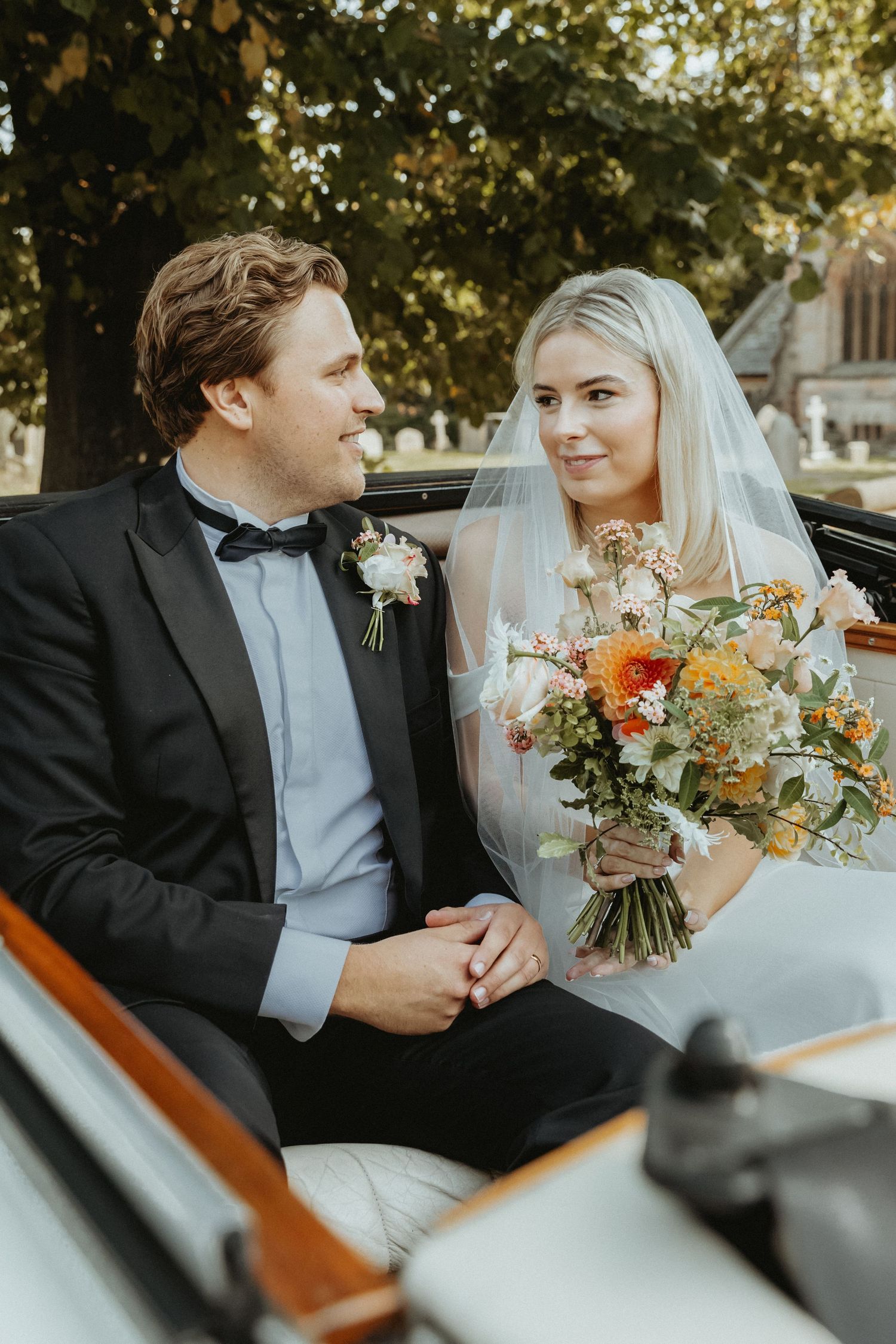 Bride and groom sat in vintage wedding car looking at one another before leaving the church for they wedding reception