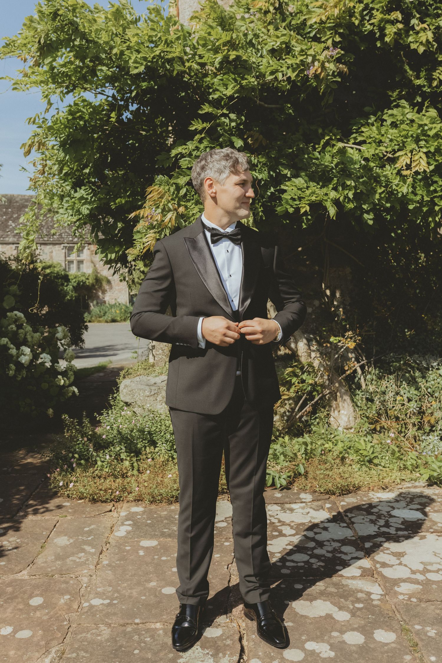Groom standing buttoning up suit jacket before his ceremony at Askham Hall