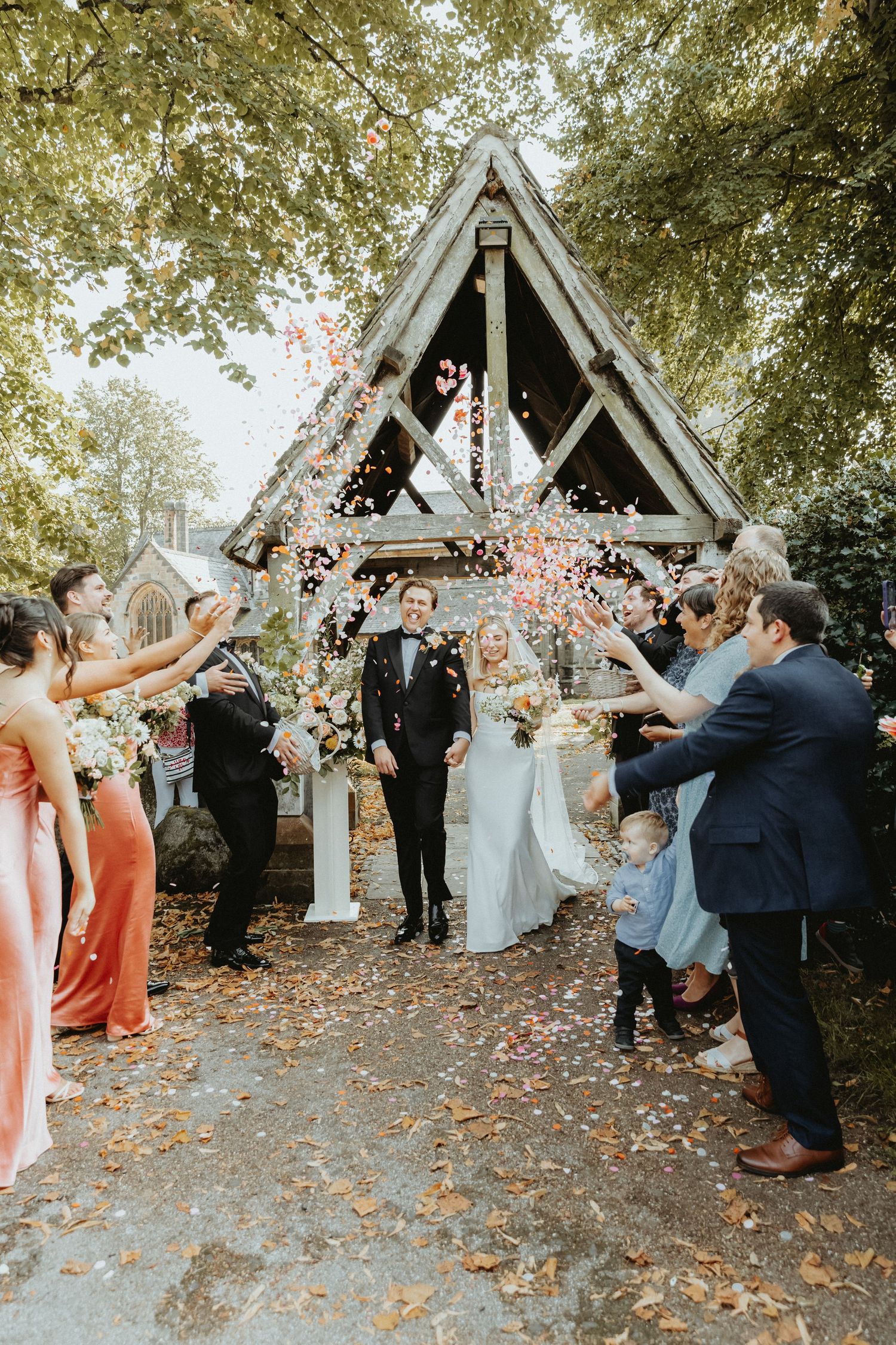 Bride and groom walking through confetti line outside St WIlfrids church mobberley after wedding ceremony