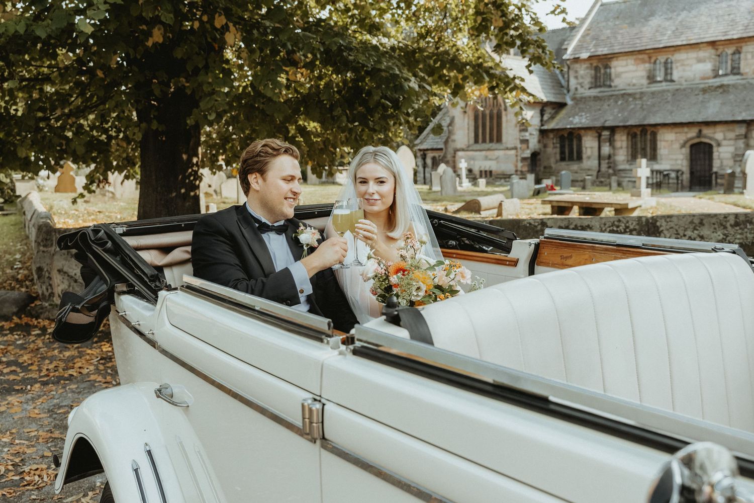 Bride and groom toasting with a glass of fizz in the back of their vintage wedding car
