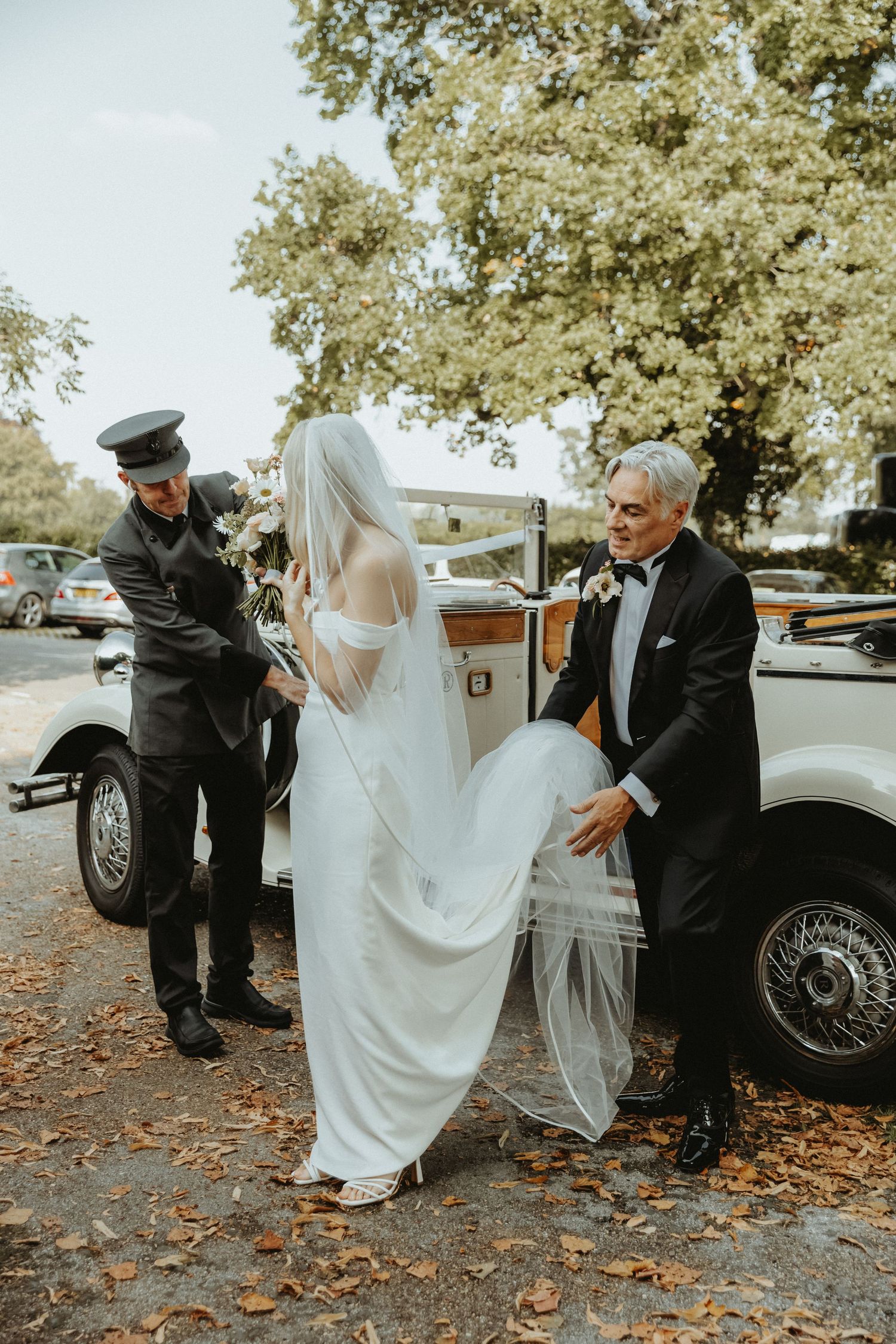 Brides dad holding brides dress as she gets out of vintage wedding car