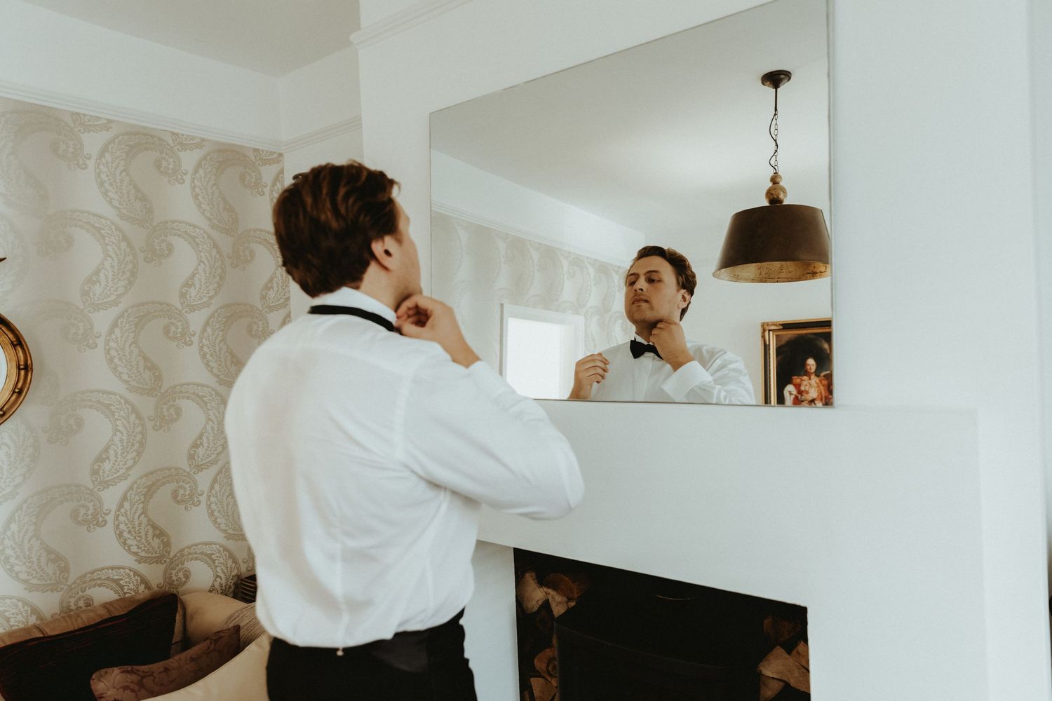 Groom putting bow tie on in the mirror during groom prep at an airbnb in Knutsford