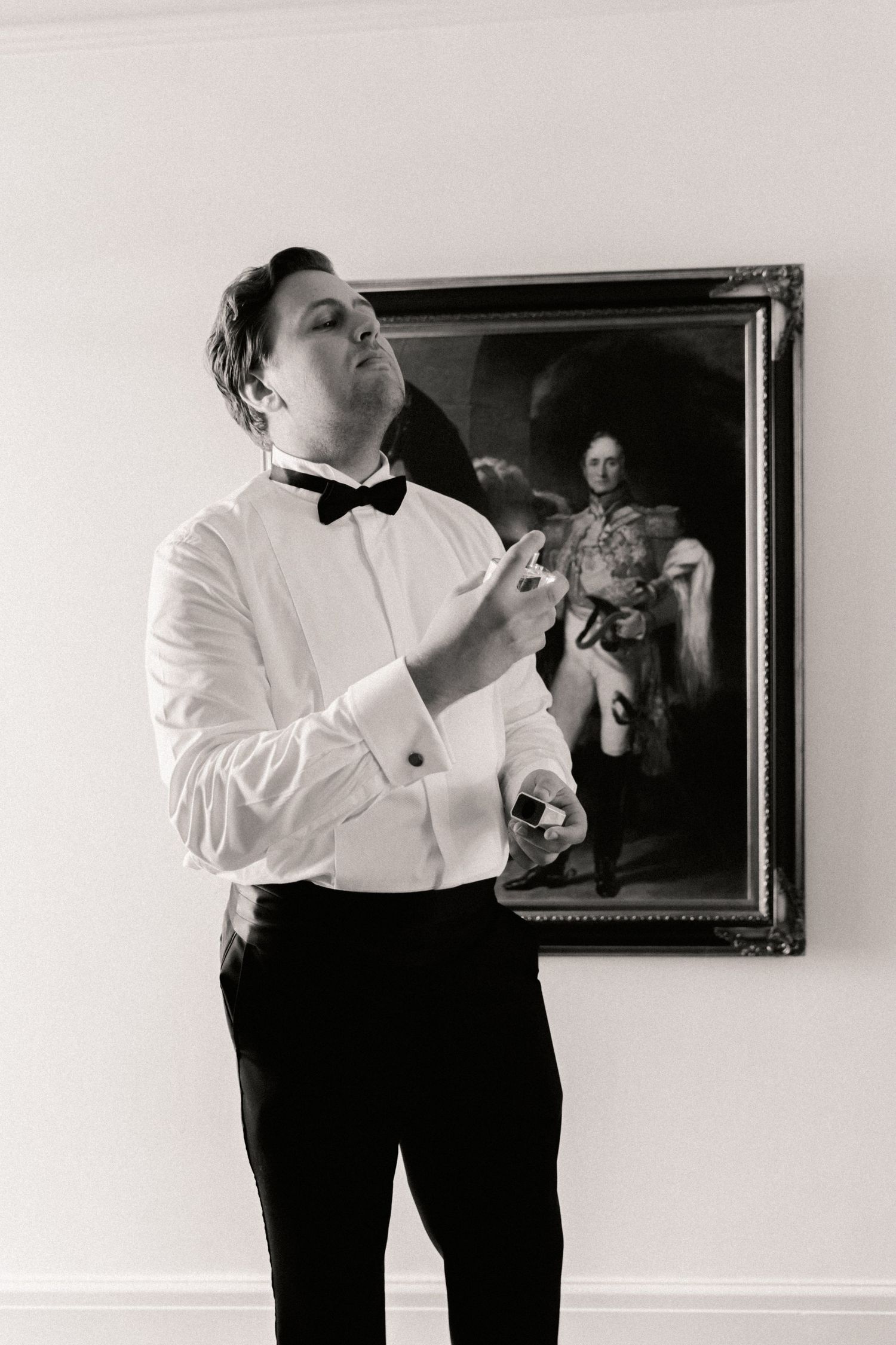Black and white image of groom spraying fragrance at groom prep