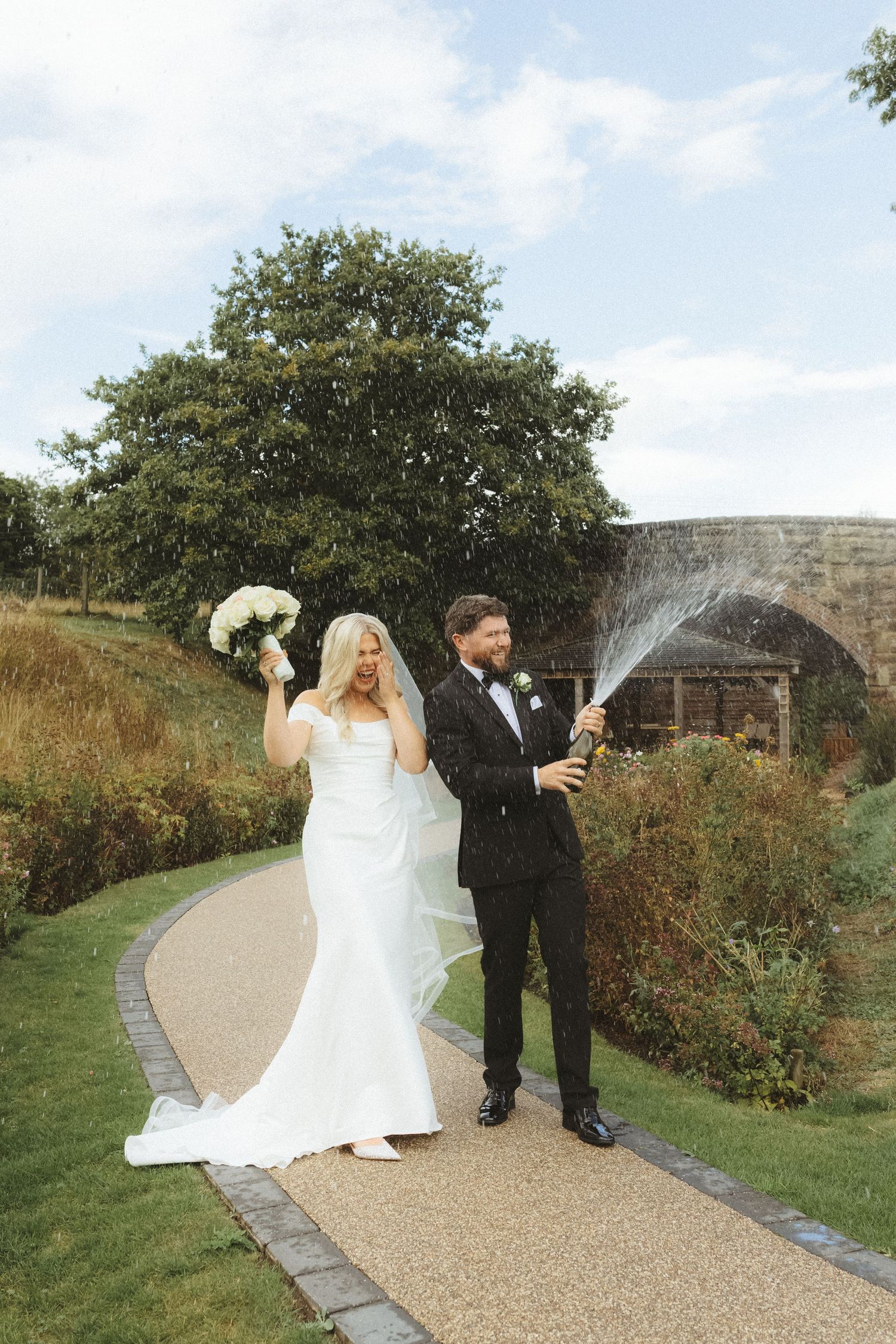Bride and groom spraying champagne on wedding day In Cheshire