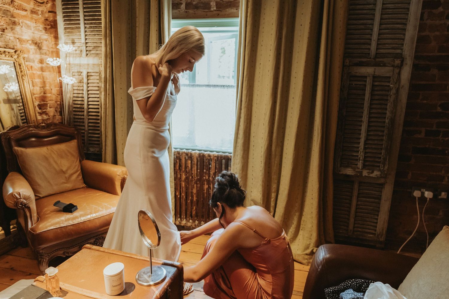 Bridesmaid helping bride into shoes during bride prep at The Roebuck Inn