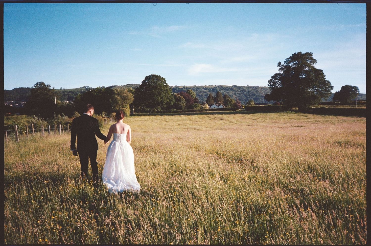 Bride and groom walking through long grass during golden hour at Tower Hill Barns in North Wales.