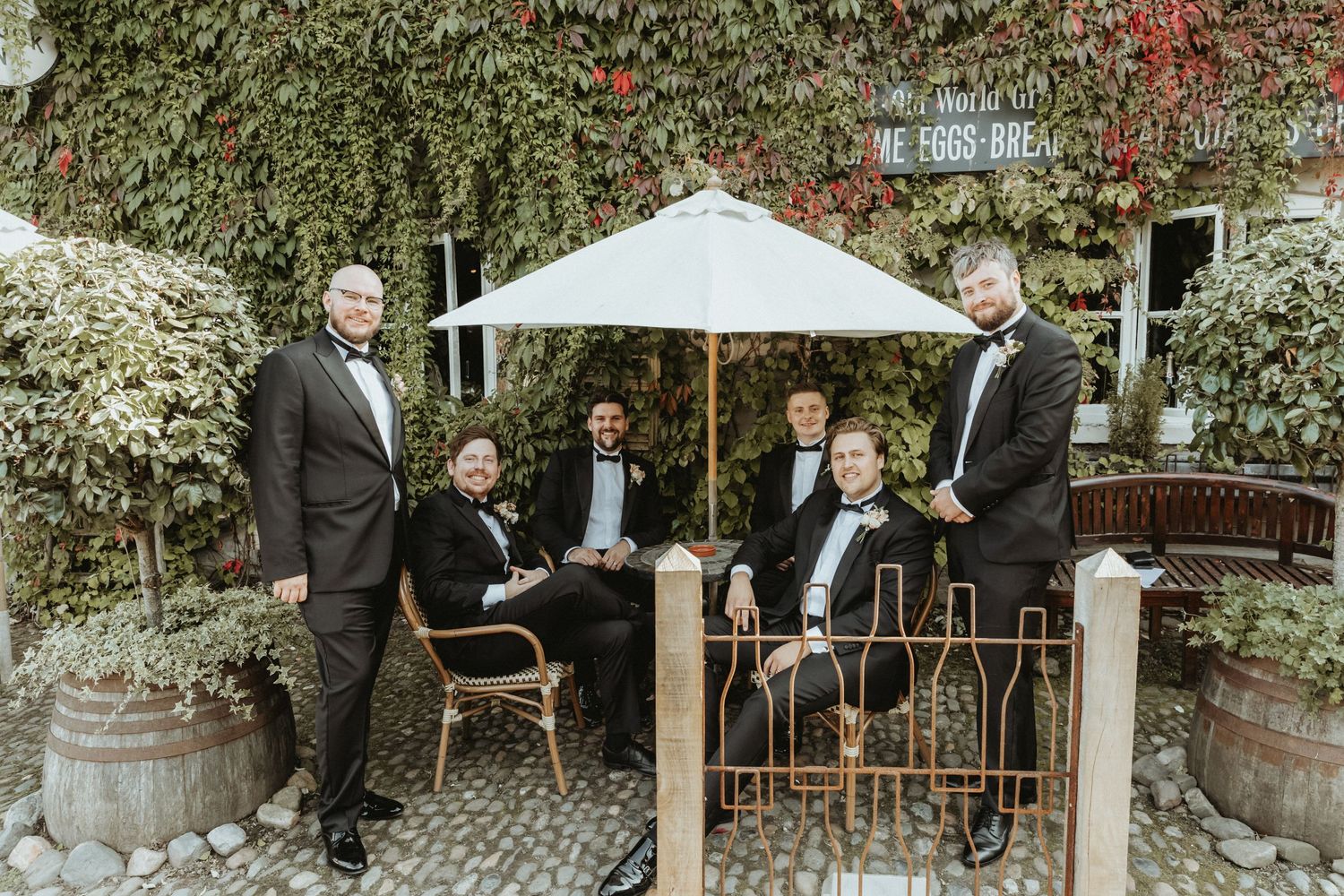 Groom and groomsmen outside Roebuck Inn with some sitting and some standing acting casual to have a 'candid' photo