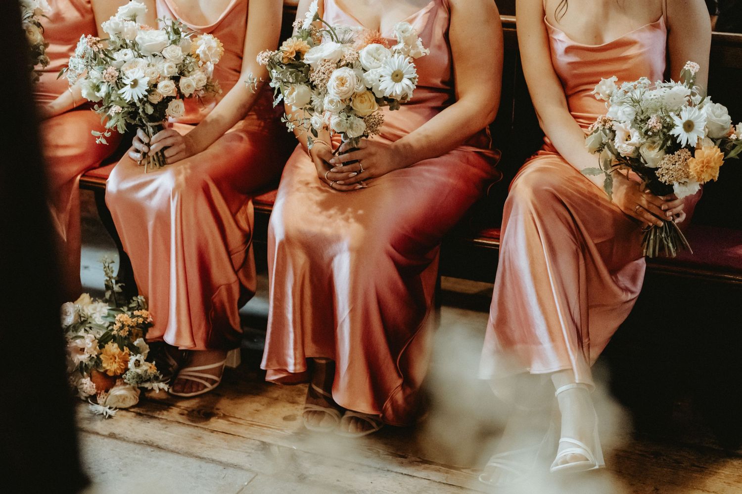 Bridesmaids sat on church pew holding bouquets