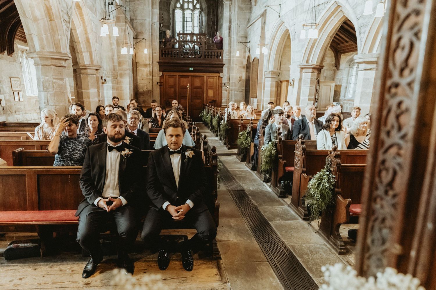 Groom and best man sat on church pew waiting for brides entrance
