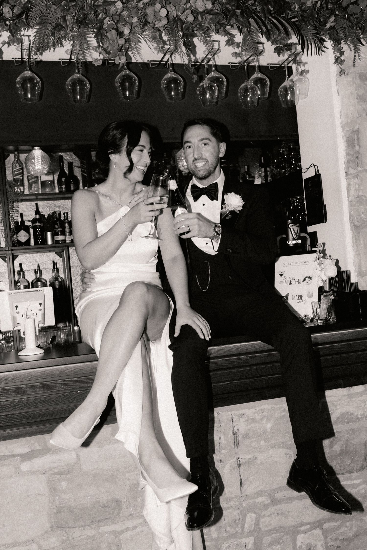 Bride and groom sitting on bar, enjoying a drink together. Photo in black and white