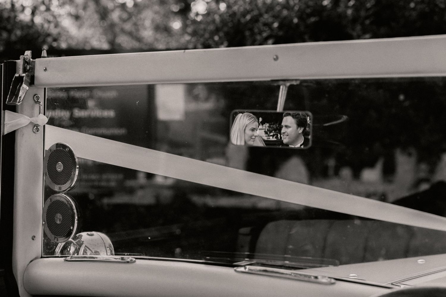 Bride and groom's face in rear mirror of vintage wedding car as they look at each other