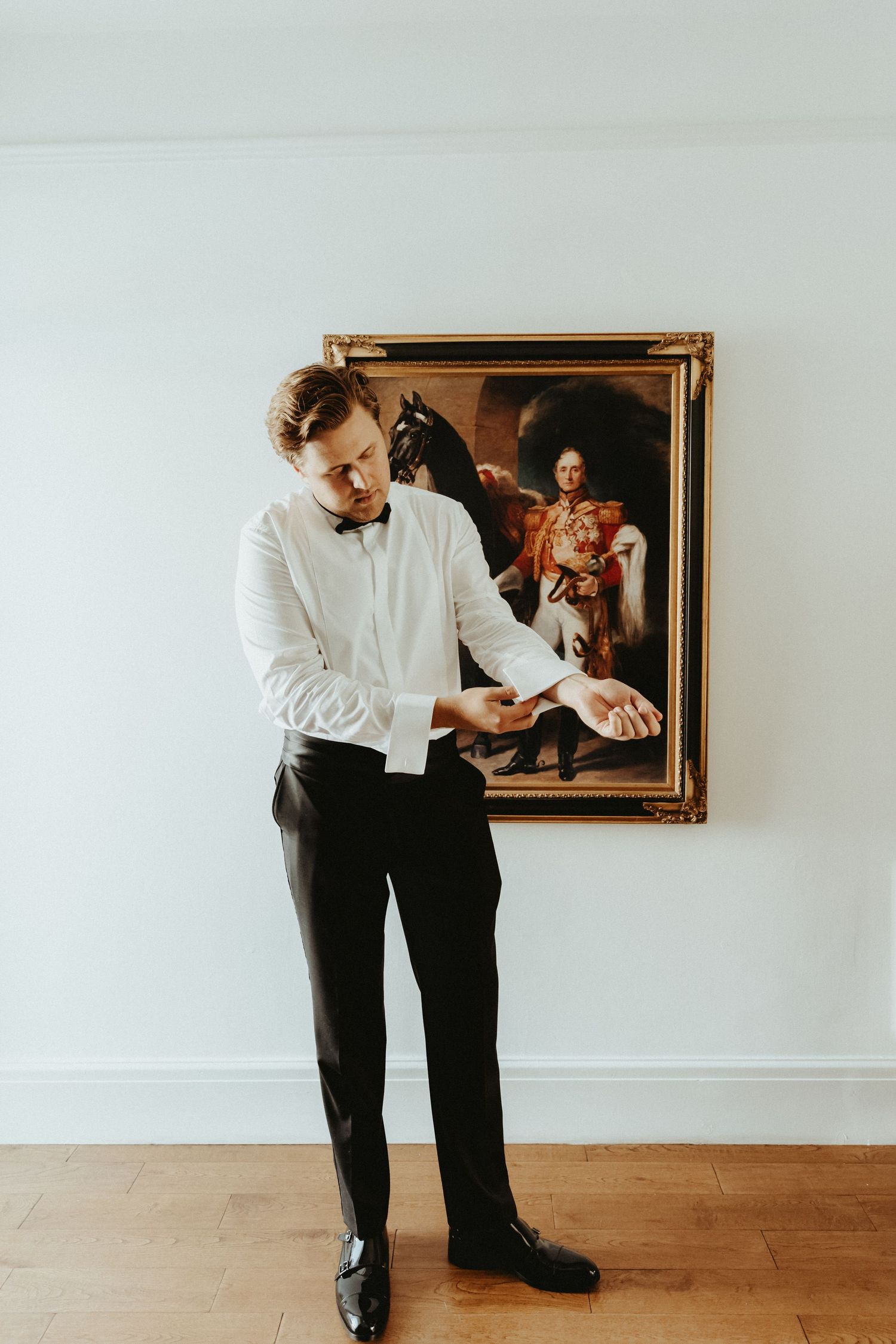 Groom standing in front of oil painting whilst putting cufflinks on