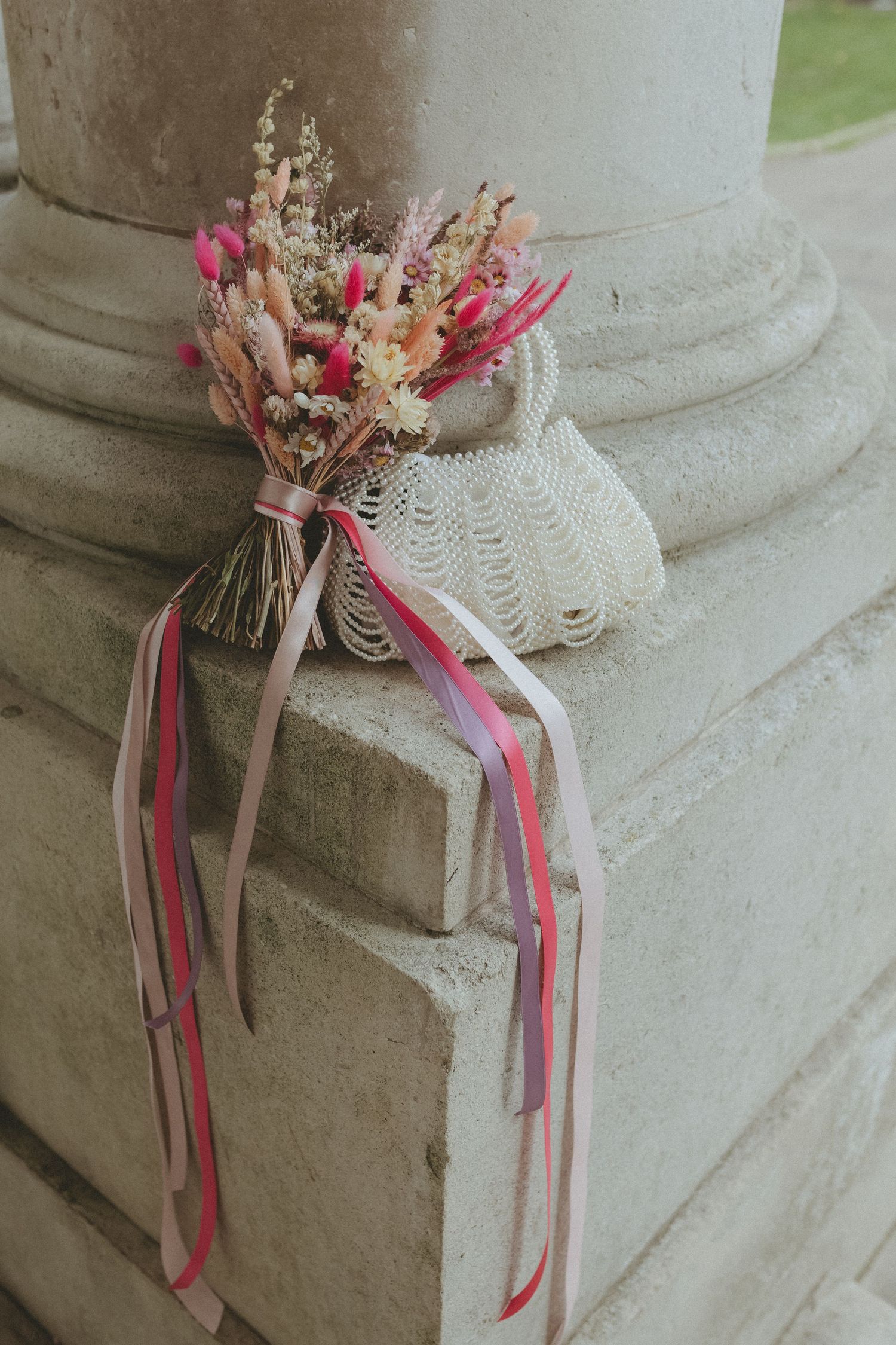 Happy Blossom dried flower wedding bouquet and wedding day pearl bag sat on stone wall.