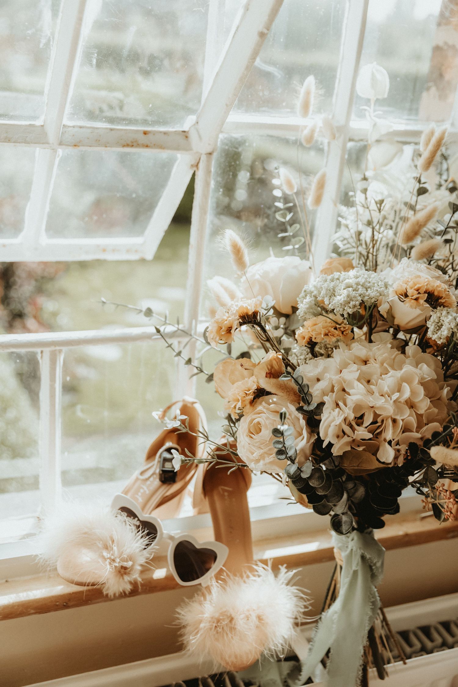 Bridal bouquet on window sill with brides shoes with sun shining through