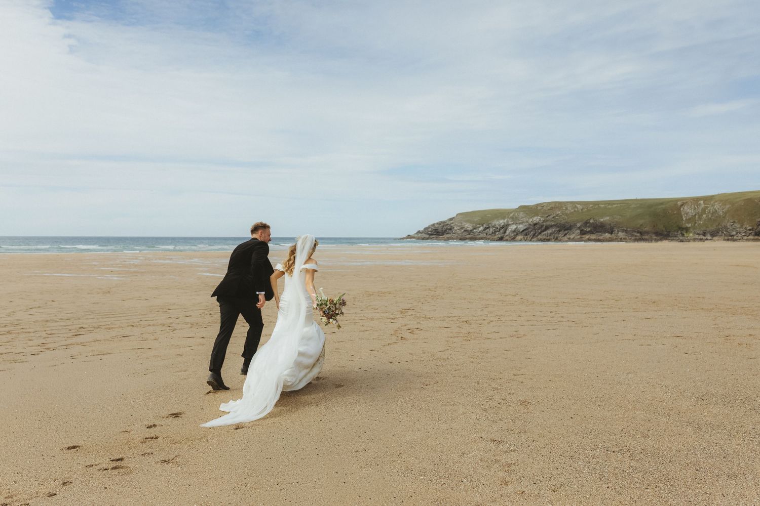 Bride and groom running across Holywell beach in Newquay Cornwall during couple portraits on their wedding day