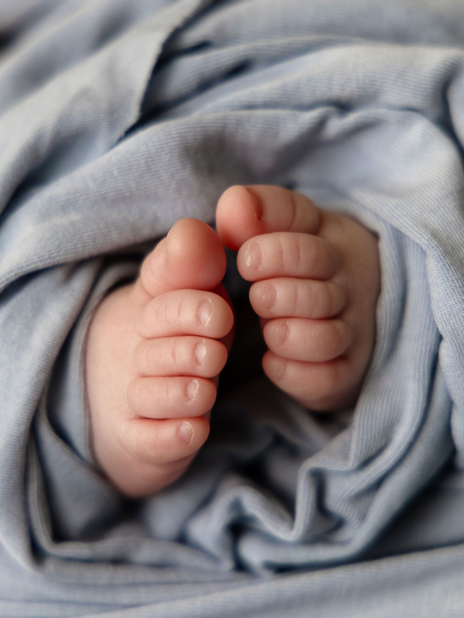 Close-up of tiny newborn baby feet peeking out from soft blue blanket.