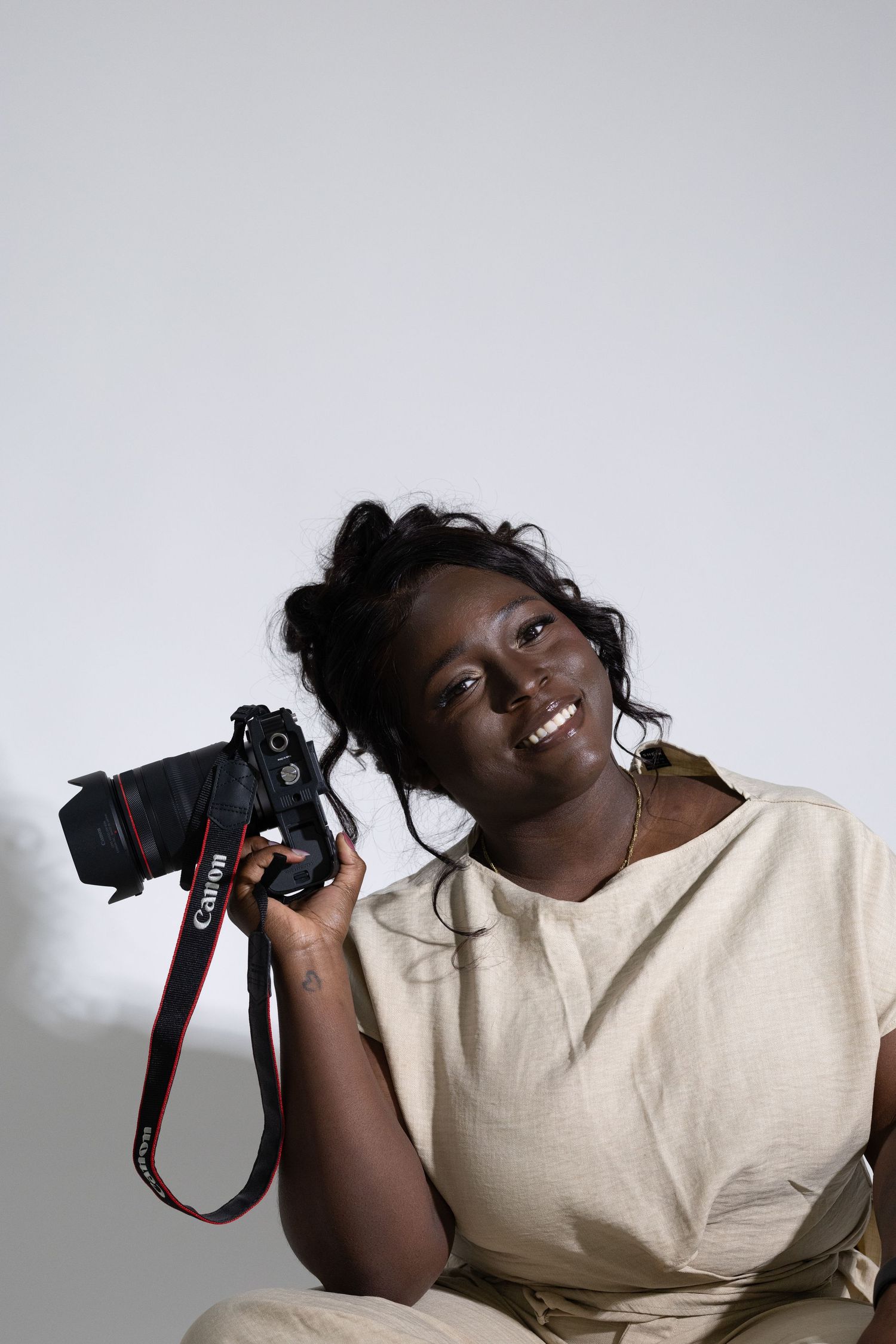 Happy smiling Black female photographer holding a Canon DSLR camera while seated indoors.