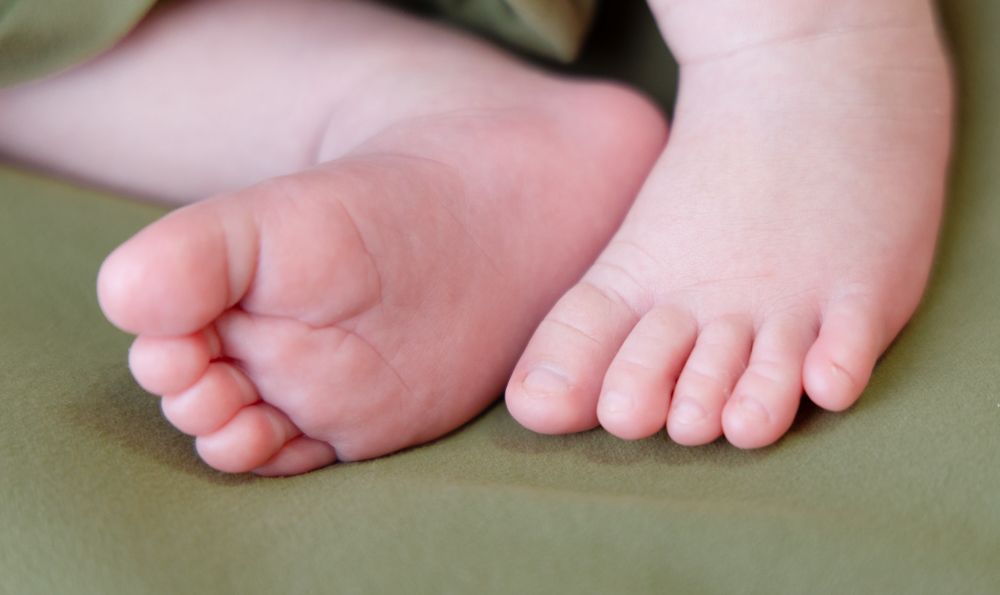 Close-up of tiny newborn baby feet and toes resting on soft green fabric during photo session.