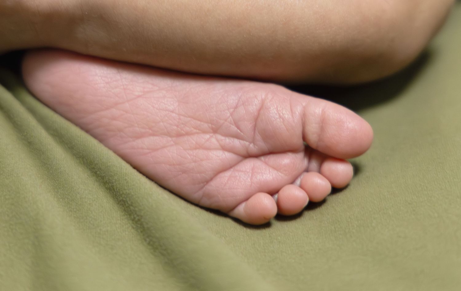 Close-up of newborn baby foot sole resting on green fabric background.