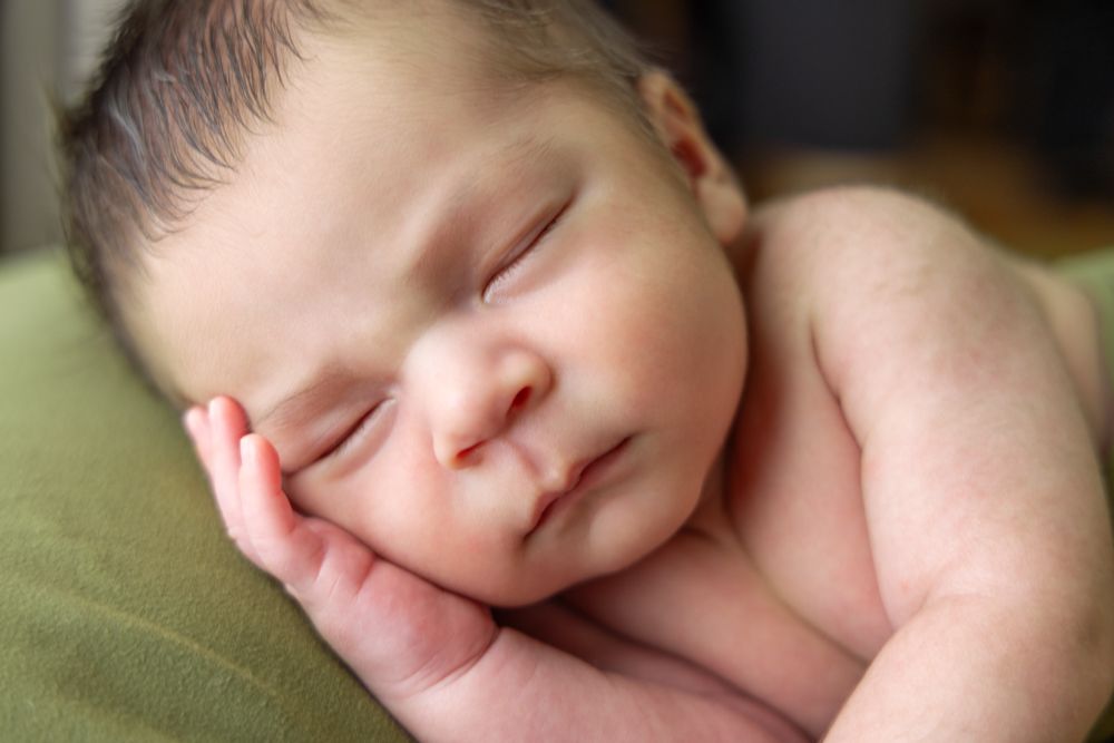Close-up of sleeping newborn baby resting on adult's hand.