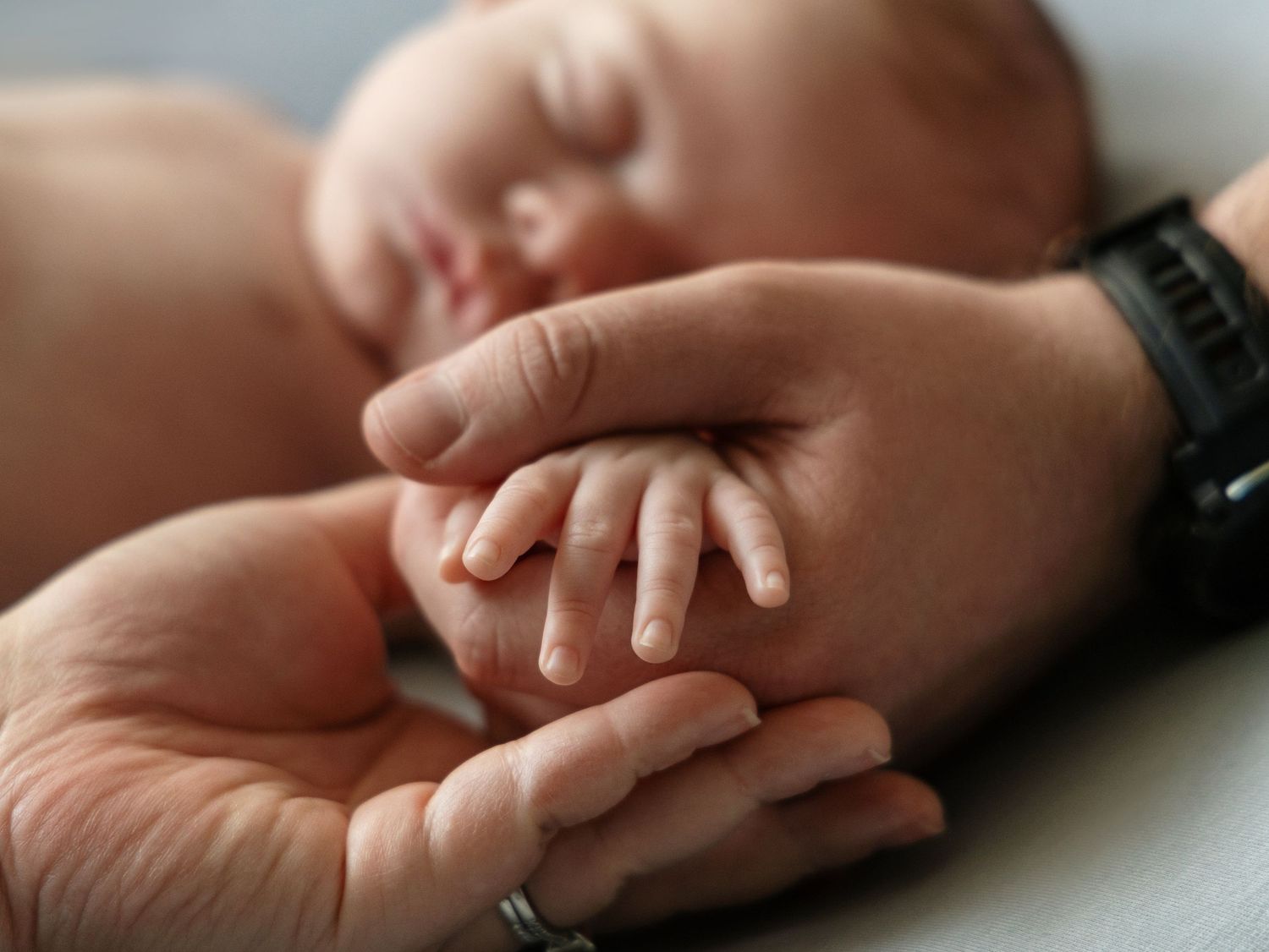 Newborn baby grasping adult parent finger in tender close-up bonding photograph.
