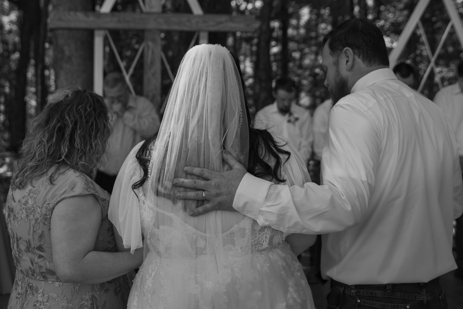 mom and dad with hands on brides back as they pray over her