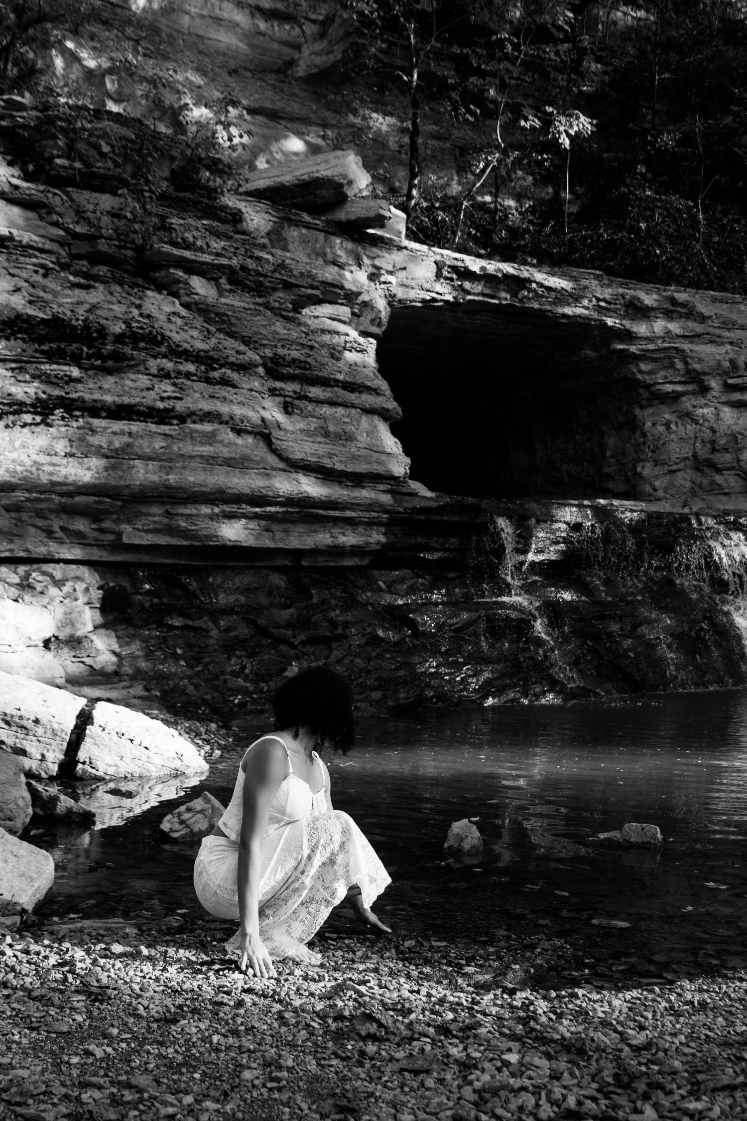 Girl leaning to down to touch the water that comes out from the waterfall.