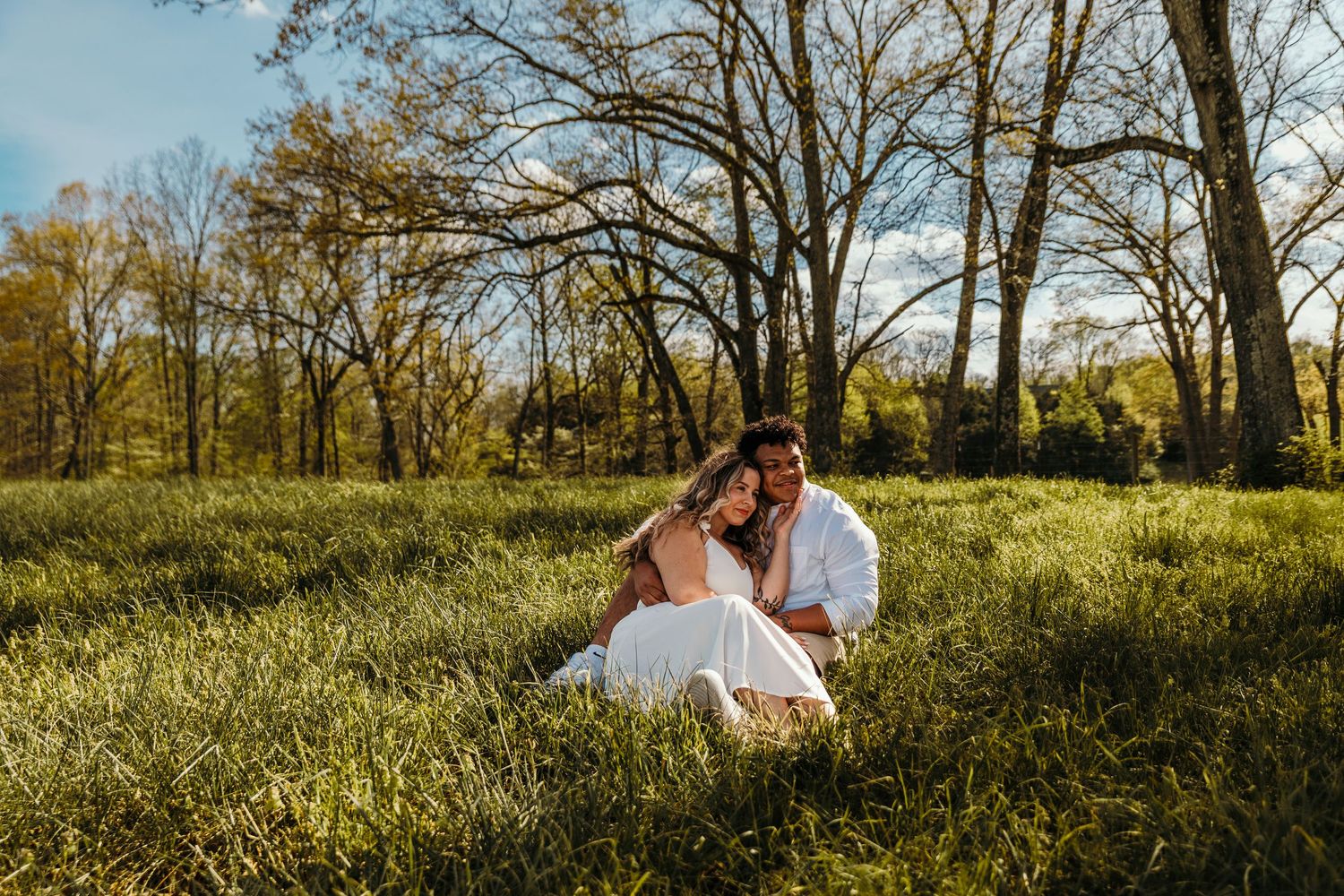guy and girl sitting in a field cuddled up