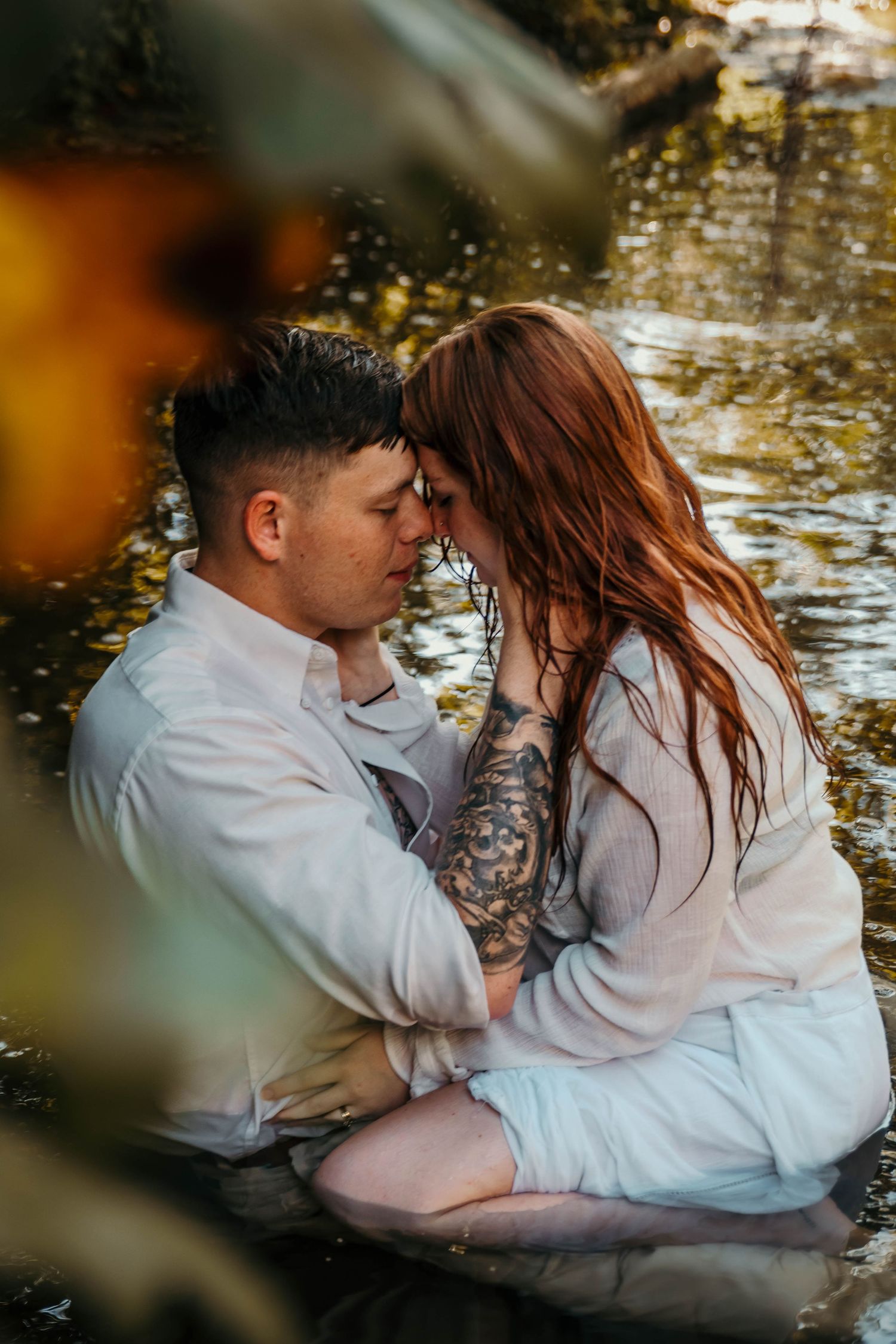 Boy and girl sitting nose to nose while sitting in a creek on a hot summer day.